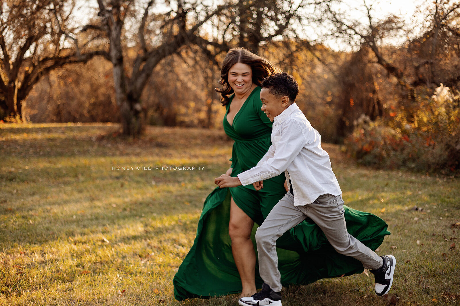 A mother in a flowing green dress holding hands with her young son as they run through an open field in Grand Rapids, Michigan, capturing a joyful and playful moment.