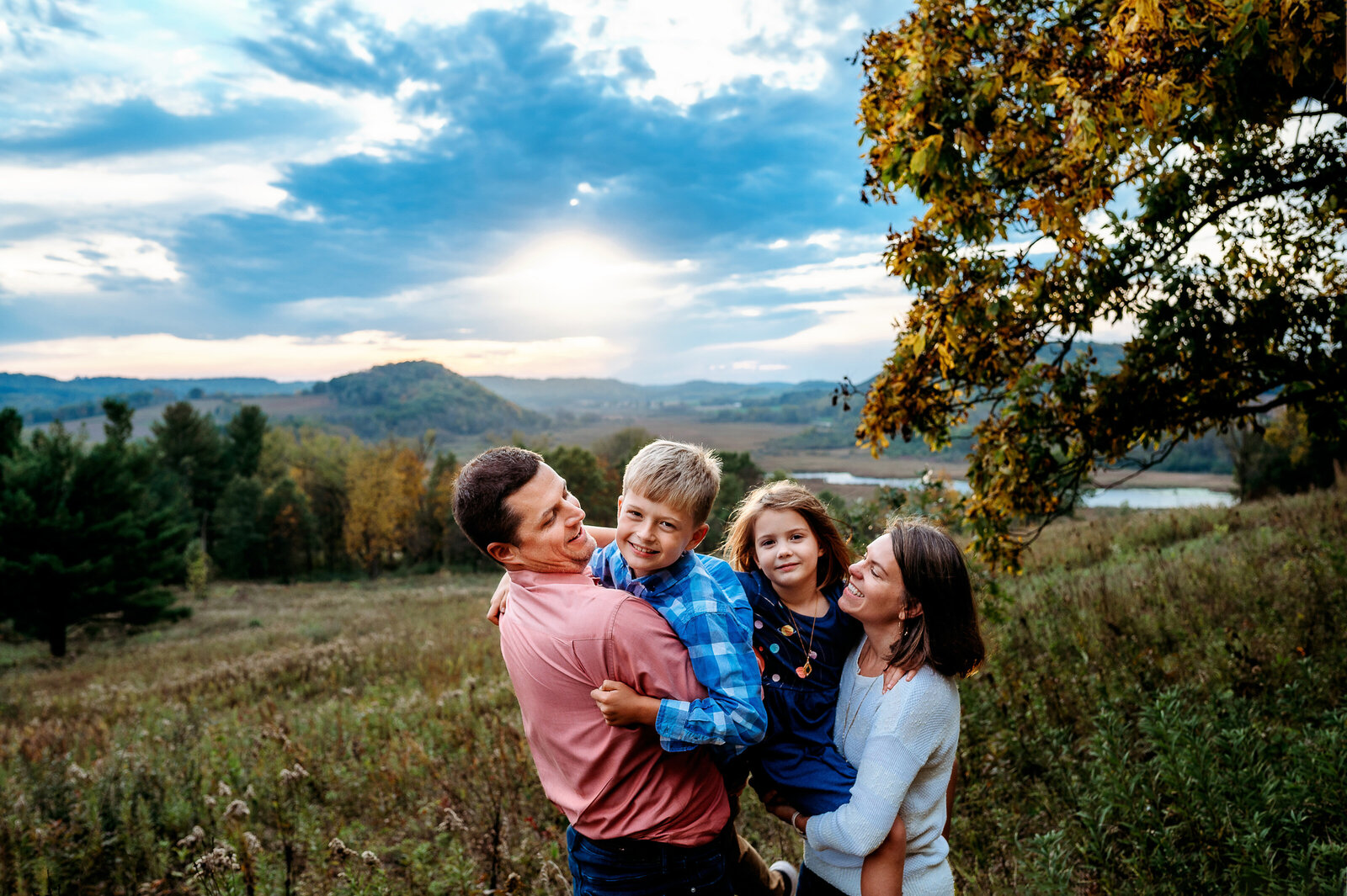 Parents holding up two kids on a hill in the fall at sunset