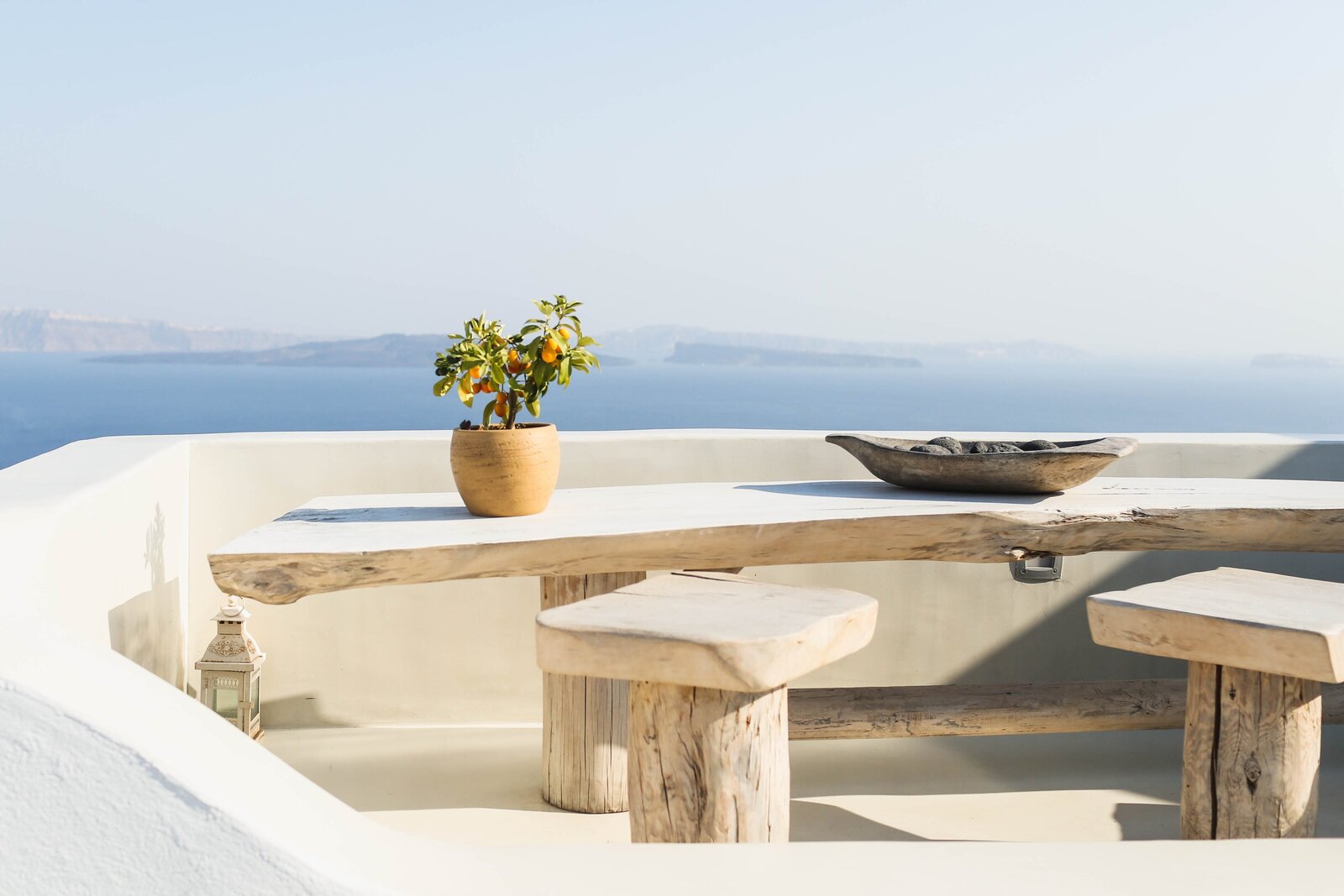 Wooden table and seat with small lemon plant and basket on table in Santorini Greece with a view of the sea in the distance 