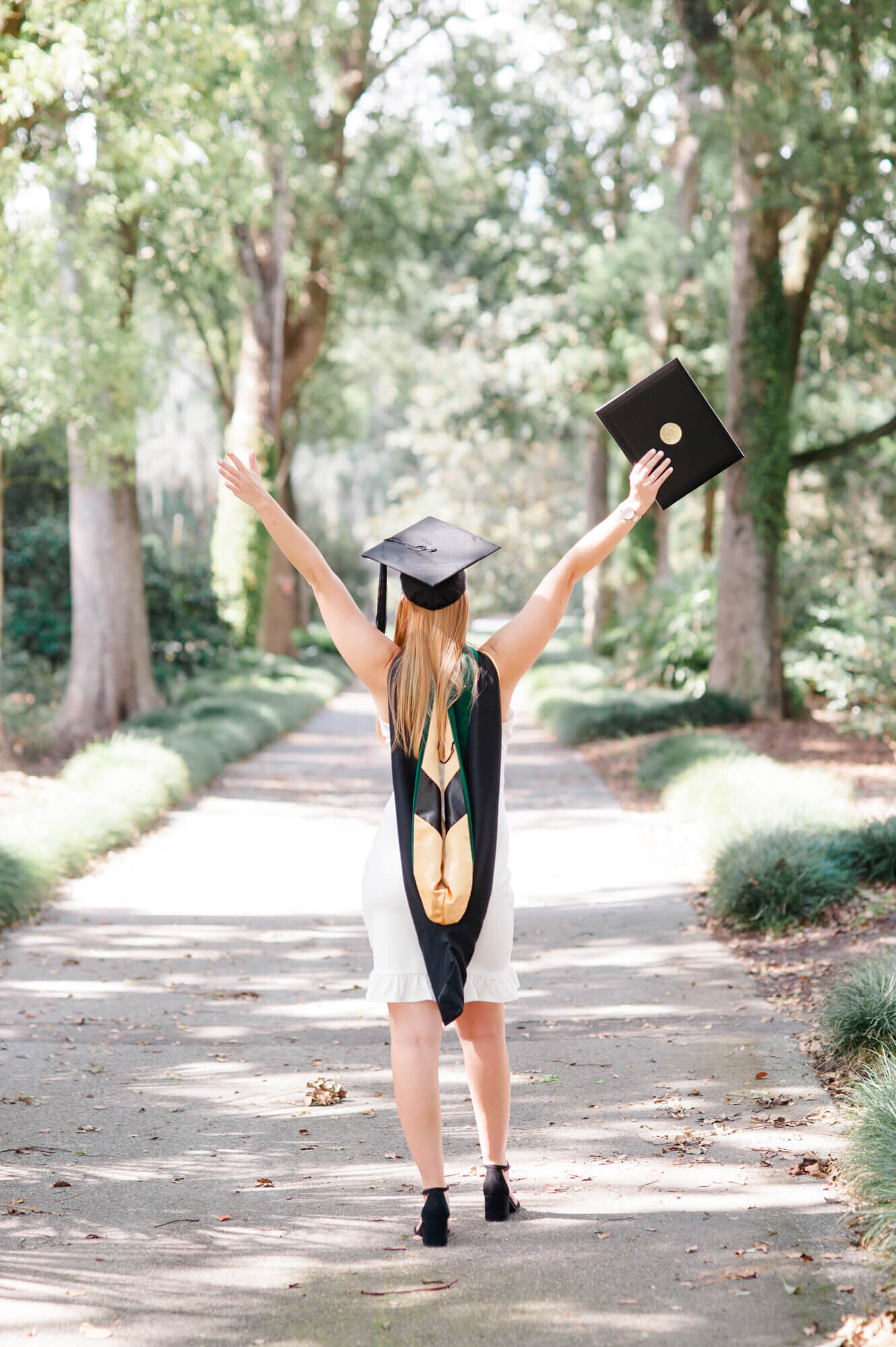 Senior throws her hands up in excitement holding her diploma during her Masters Grad session for UCF
