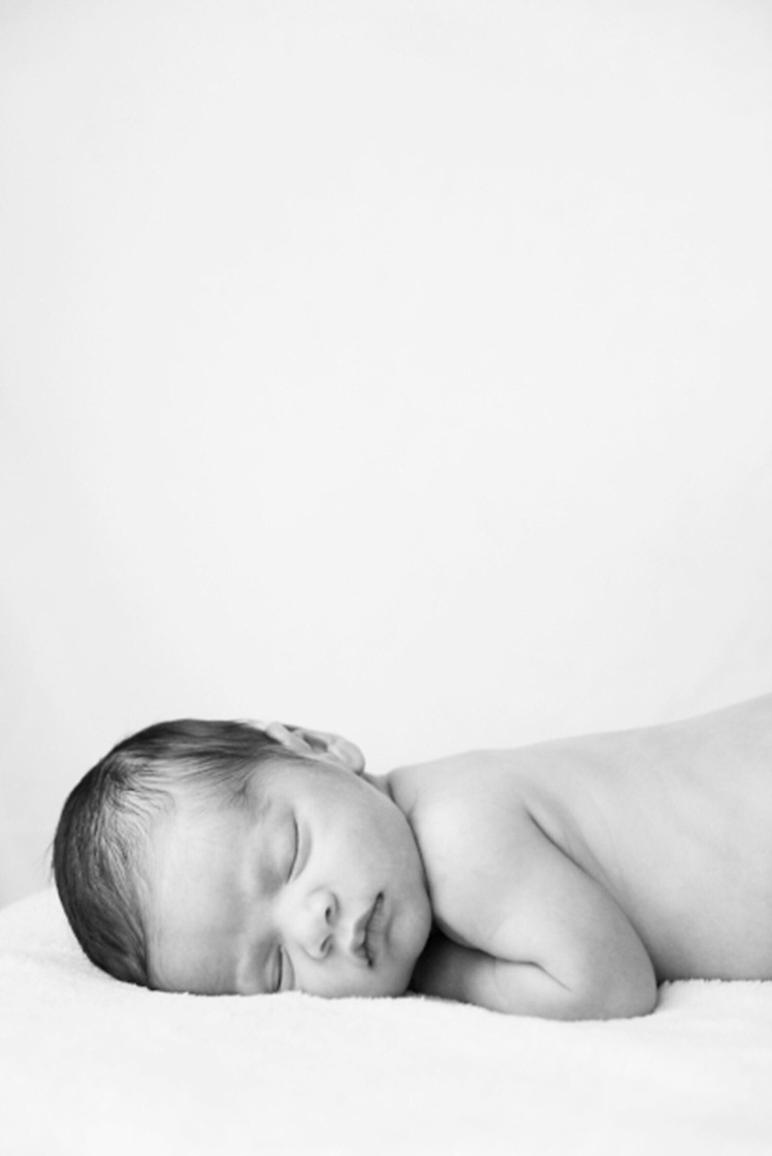Black and white portrait of a newborn baby sleeping on their stomach with head resting on folded arms, captured by a natural in-home newborn photographer in Los Altos

