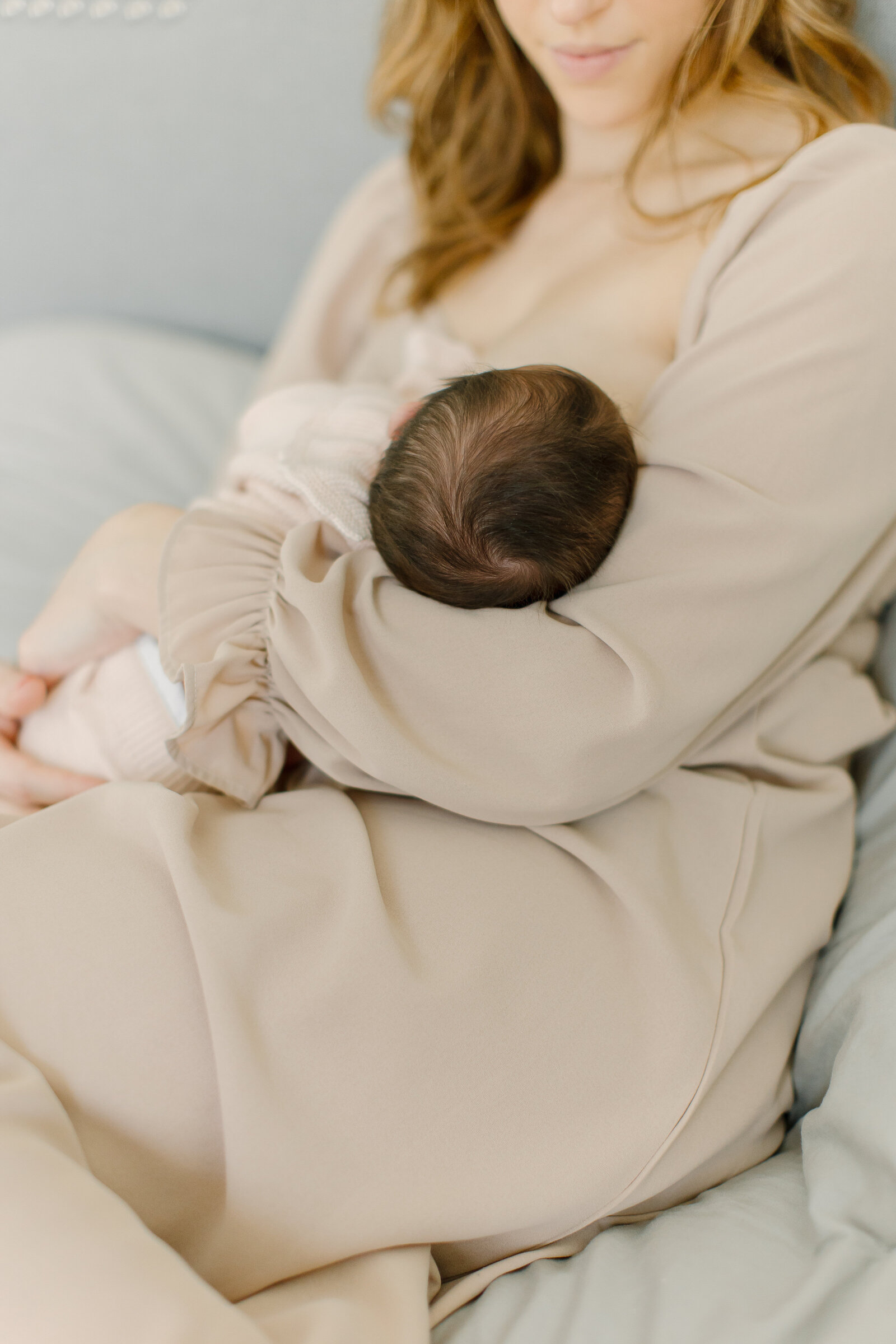 A newborn baby is breastfeeding while the mother sits on the bed