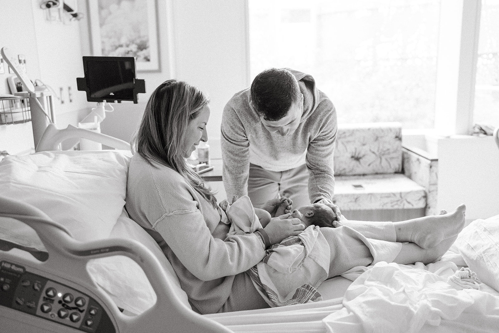 mom and dad looking at baby in hospital bed
