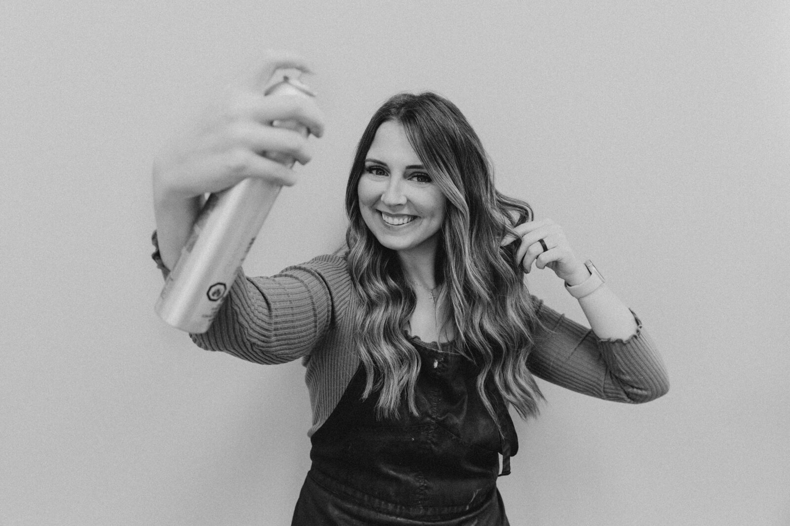 Black and white branding photo of a smiling Michigan hairstylist using hairspray, captured during a professional branding session for entrepreneurs in the Midwest.