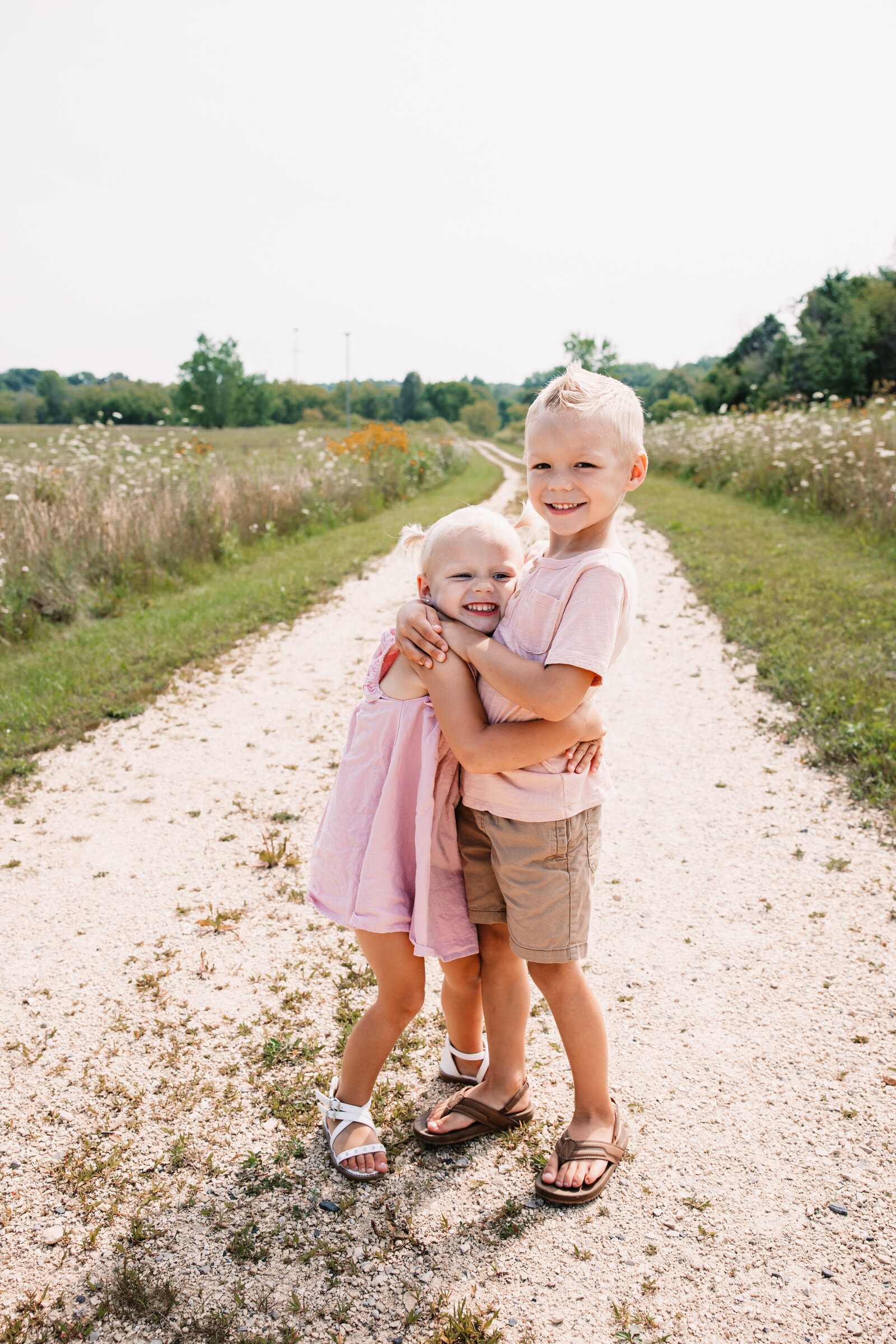Toddler boy hugs his younger sister as they stand in a park trail
