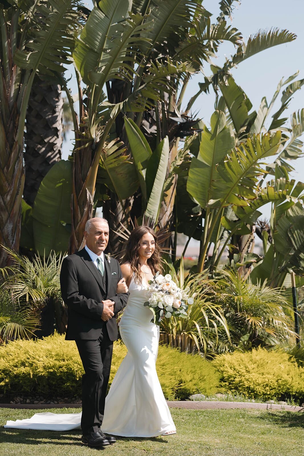 Bride walking down the aisle with her dad past palm trees