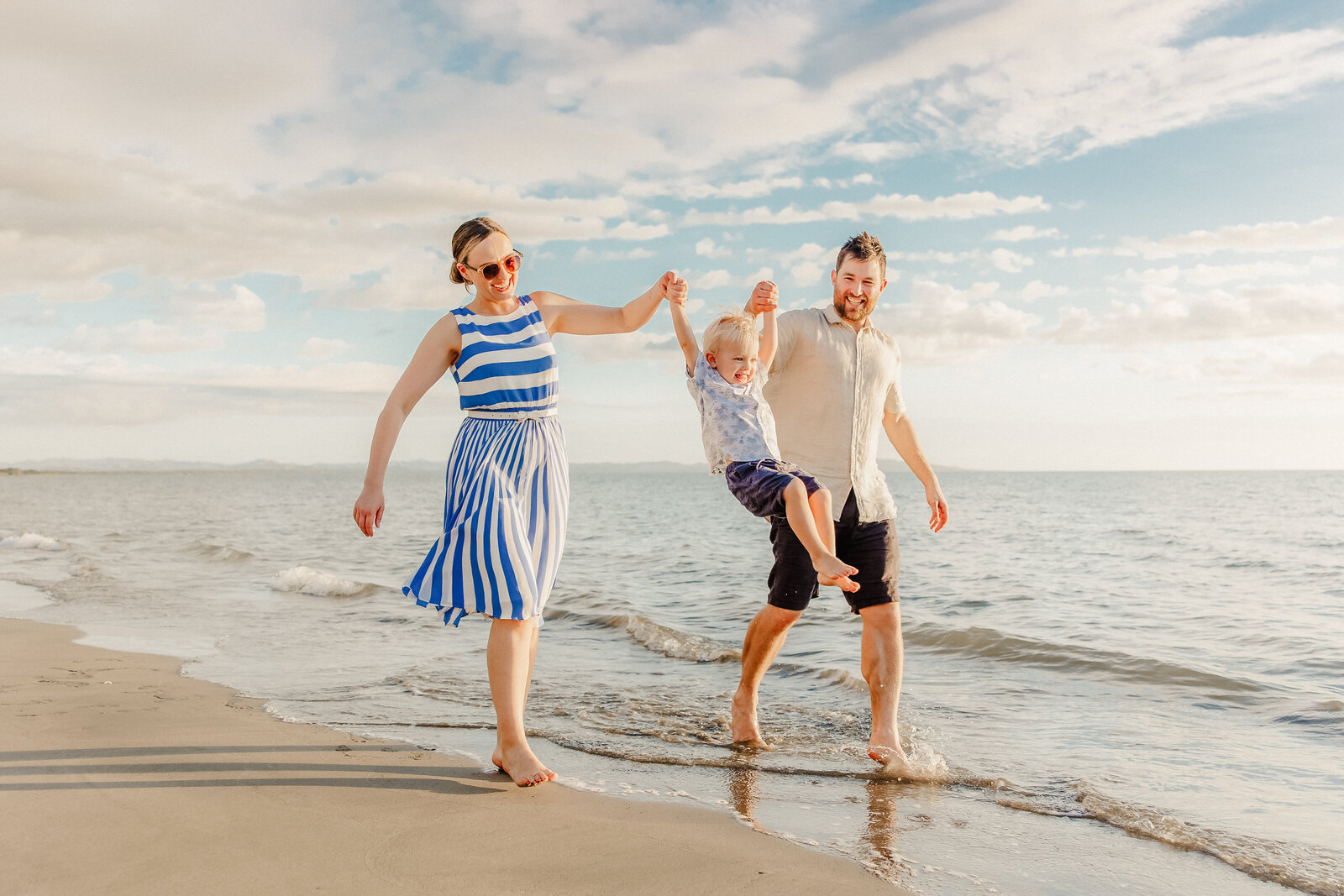 family hand in hand walking down the beach, swinging their child