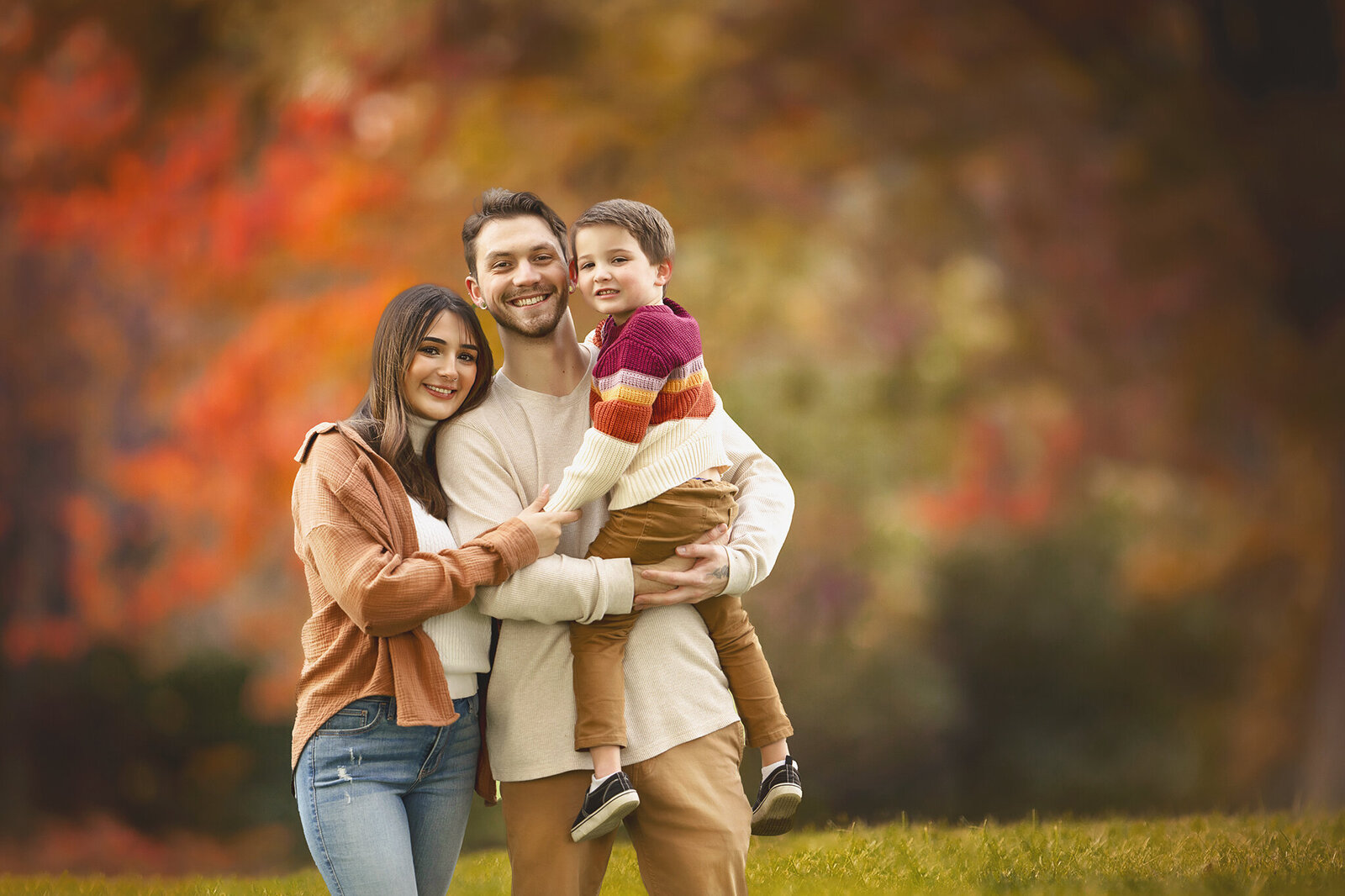 Couple with boy standing at the park with fall trees