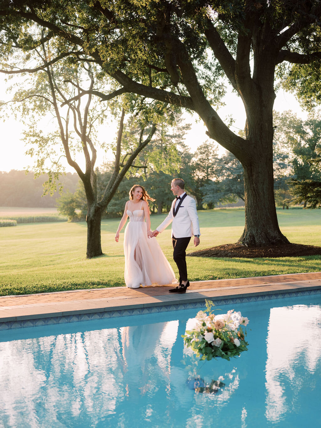 Bride and groom walking beside the pool at Brittland Estate with floral arrangement floating.