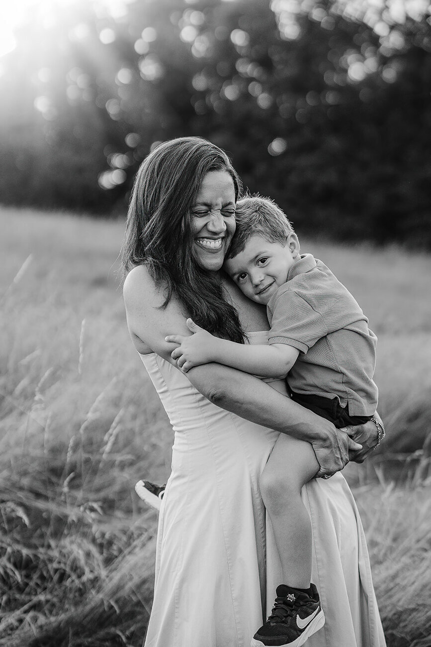 black and white portrait of a mother squeezing her son tight in a sunset field