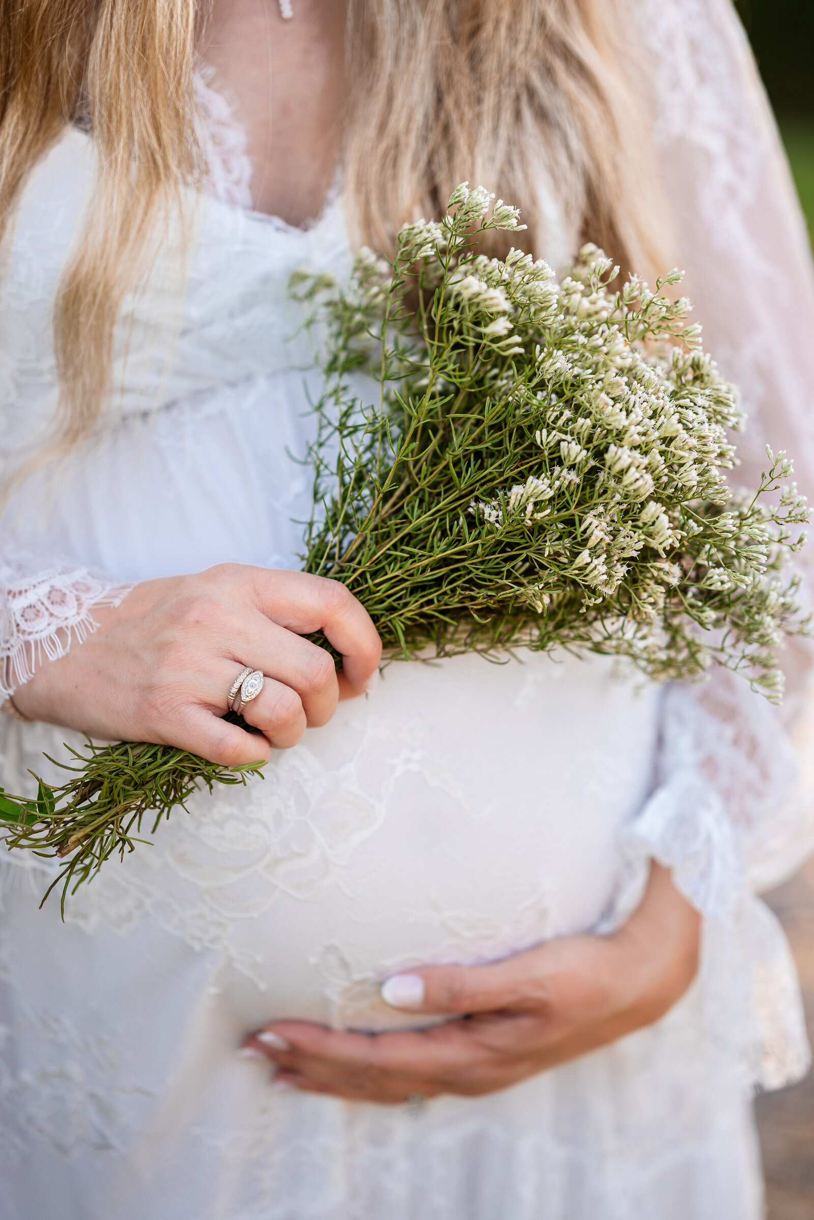 A pregnant woman with her hands on her stomach and holding a bouquet of flowers for her maternity photos in Huntsville Alabama