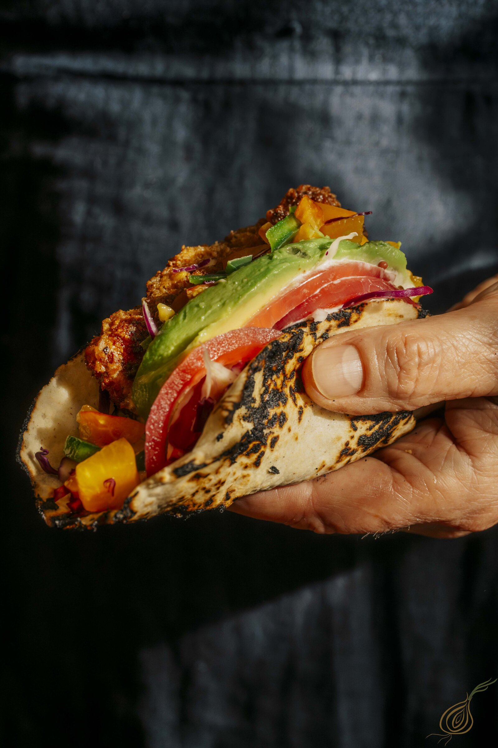 A taco filled with an abundance of toppings is held by a person, emphasizing the meal's enticing presentation.
