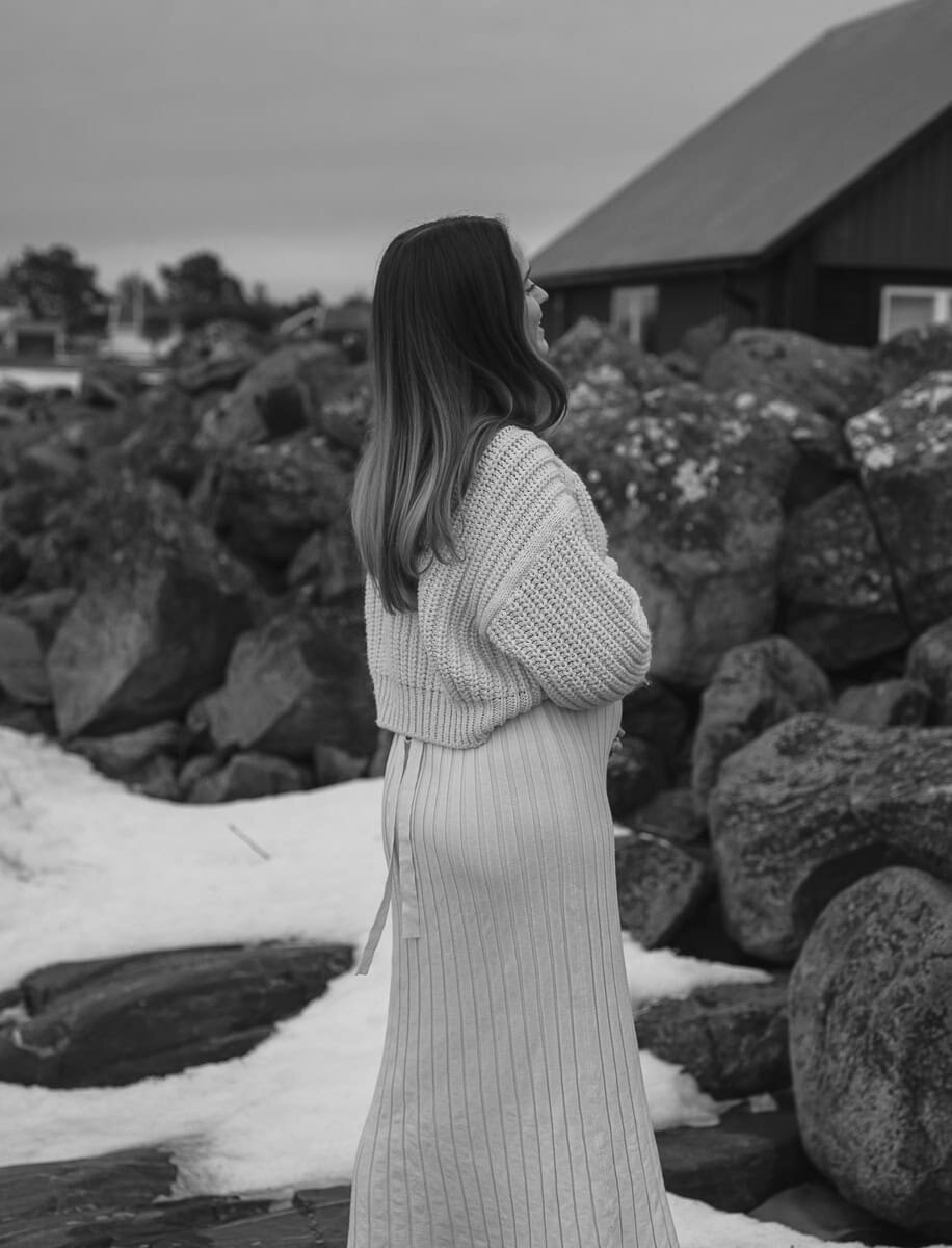 Gravid kvinna håller om sin mage och ler avslappnat i stockade kläder.