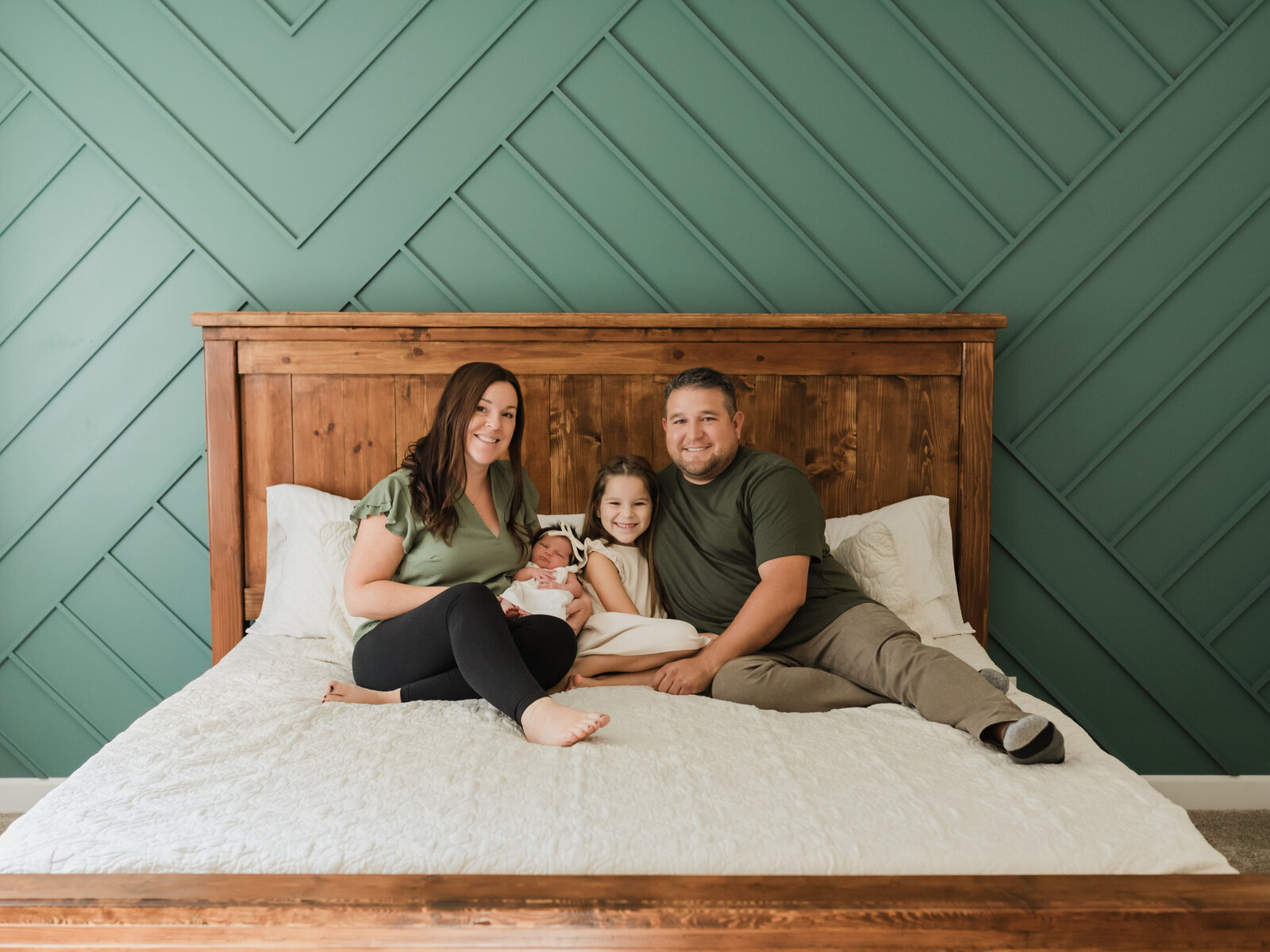 family sitting on bed holding newborn baby girl for in home lifestyle session cleveland newborn photographer