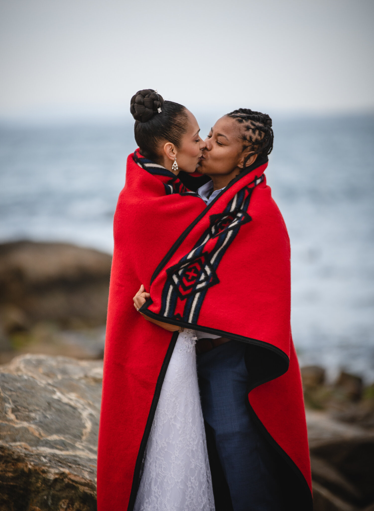 two brides kissing with red blanket on beach