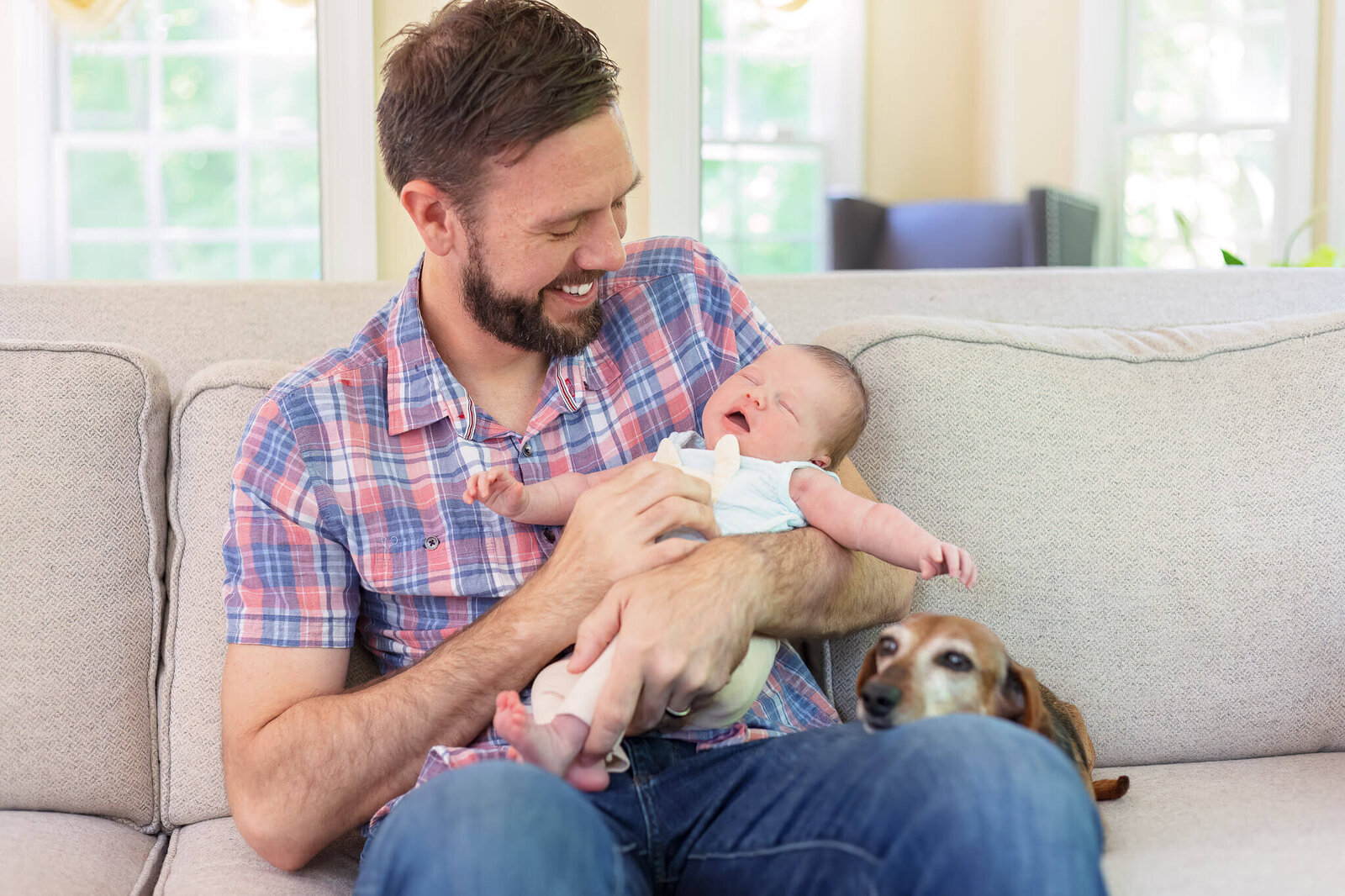 A dad holding his newborn daughter with the dog sitting next to them.