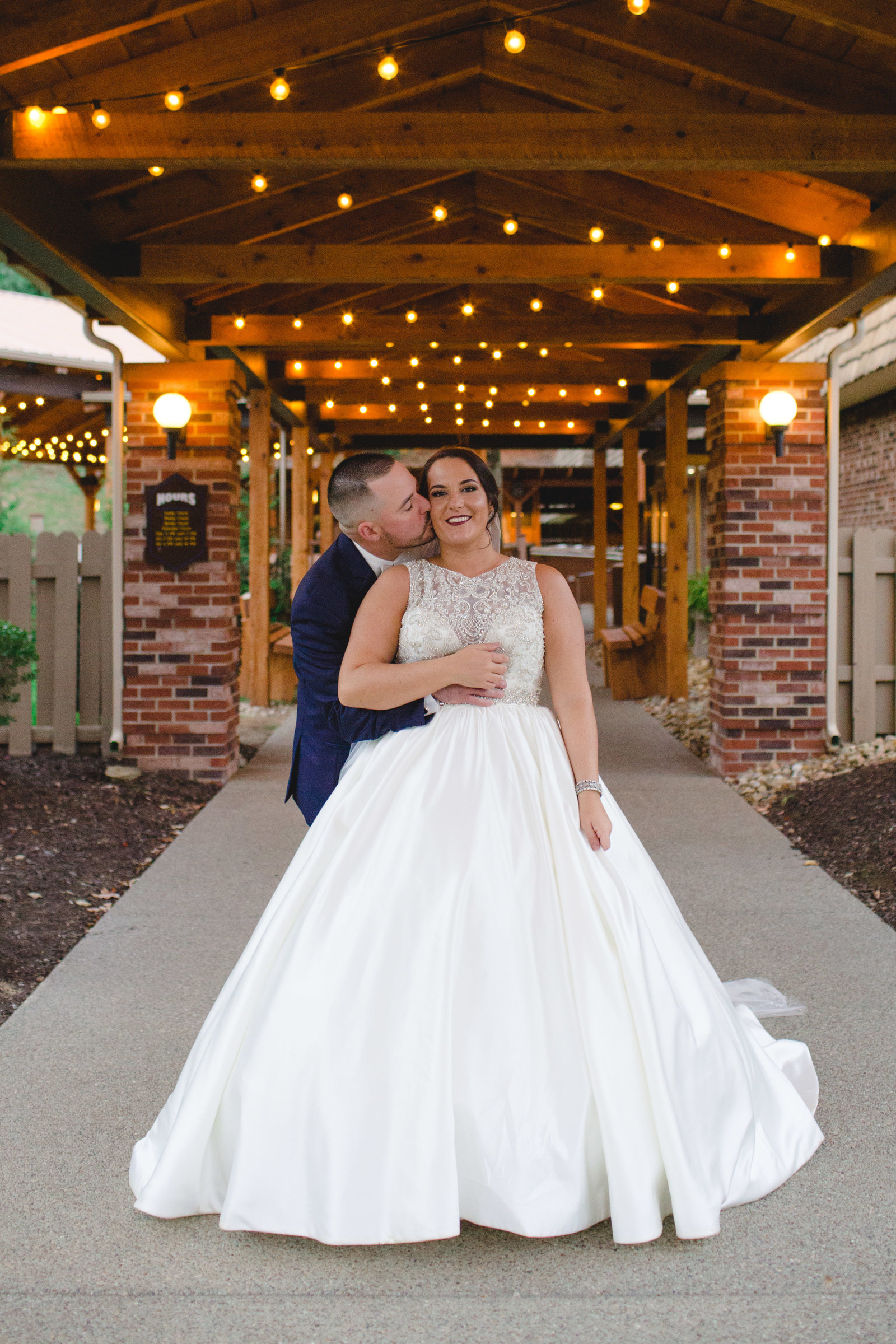 groom sneaks up on bride and kisses her cheek under the twinkle lights at the chadwick