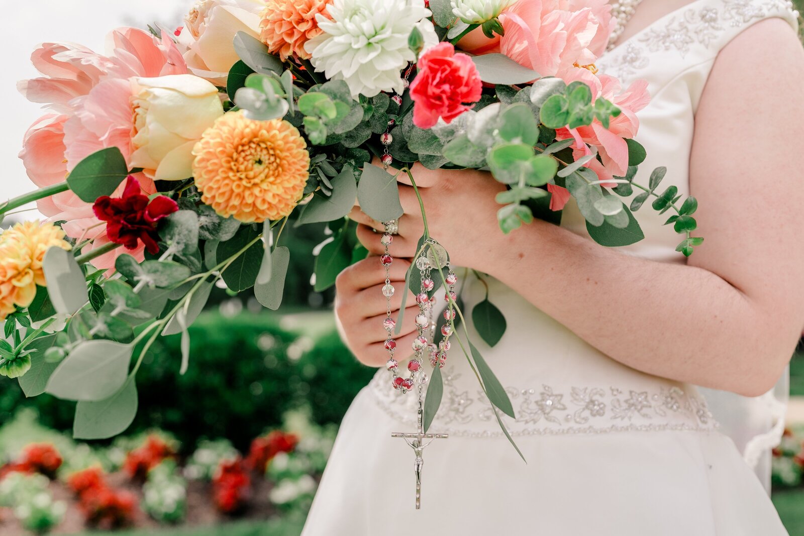 A bride holding her bouquet of colorful flowers with a rosary wrapped around the base during a Catholic wedding in Northern Virginia