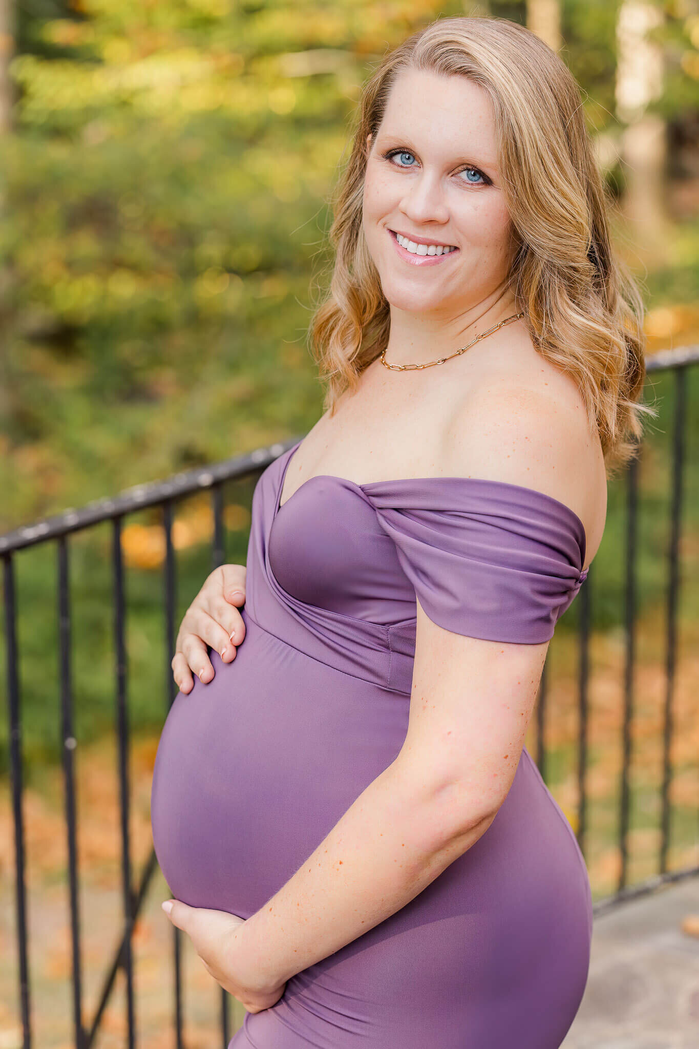 An expecting woman in a purple dress hugging her belly at a park in Northern Virginia.