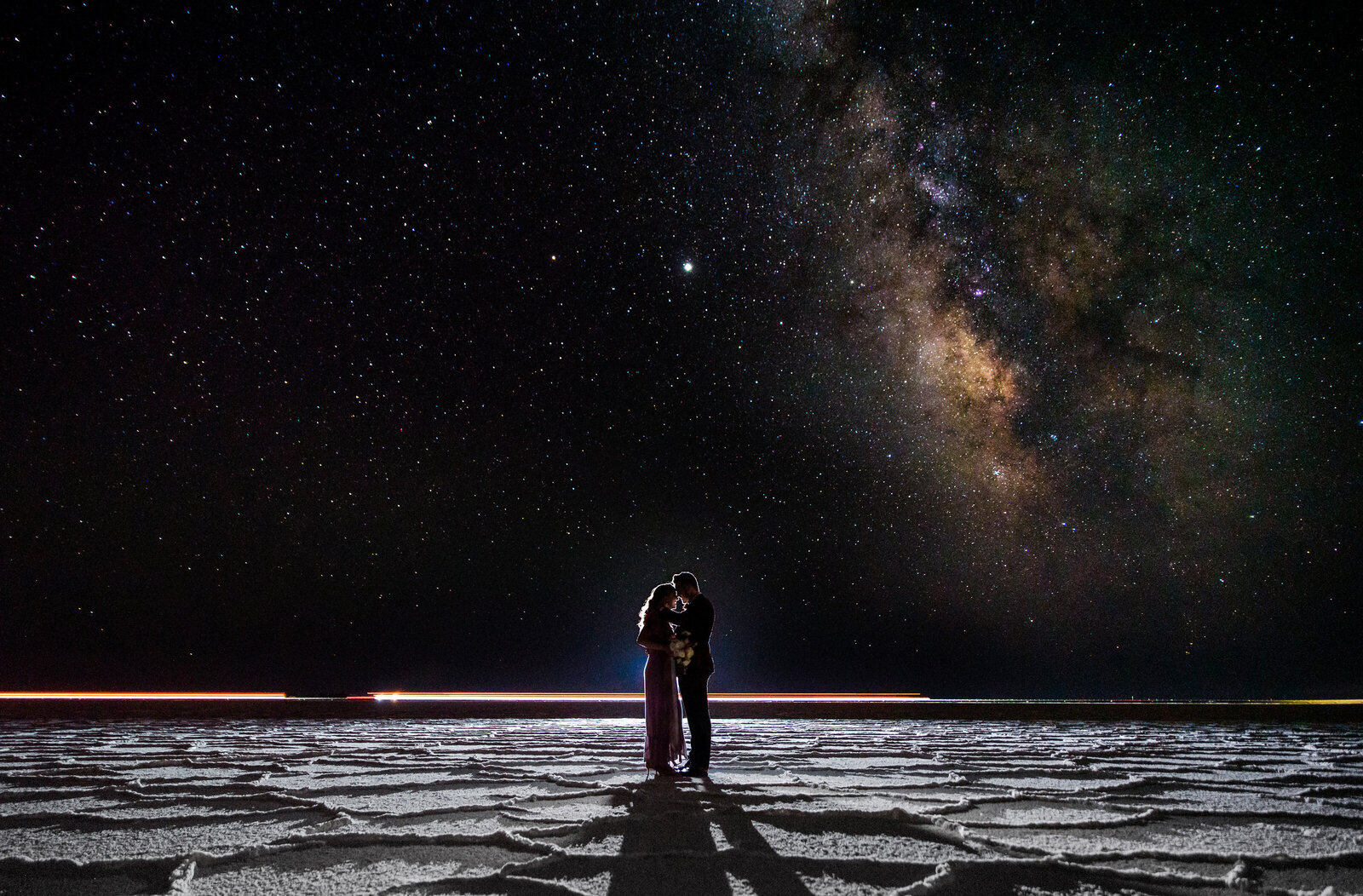 Couple standing on the Salt Flats underneath the stars and Milky Way for an anniversary session.