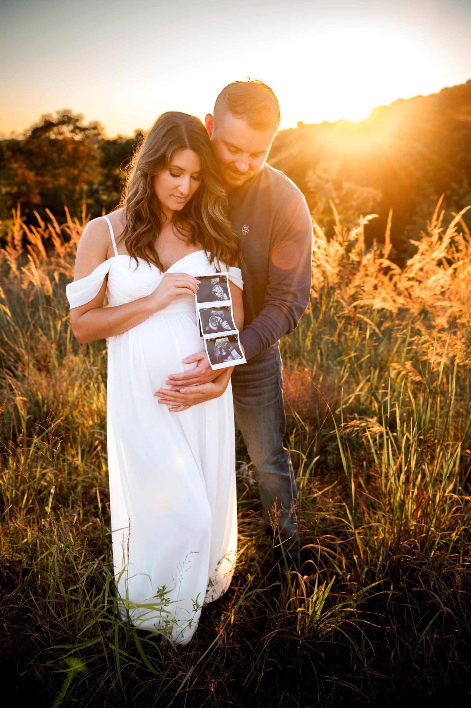 couple holding ultrasound in a field at sunset