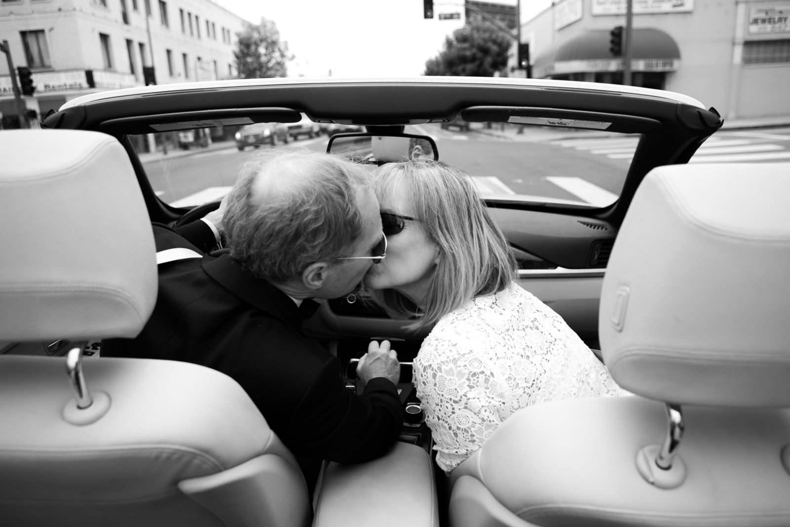 black and white photo of bride and groom kissing in convertible
