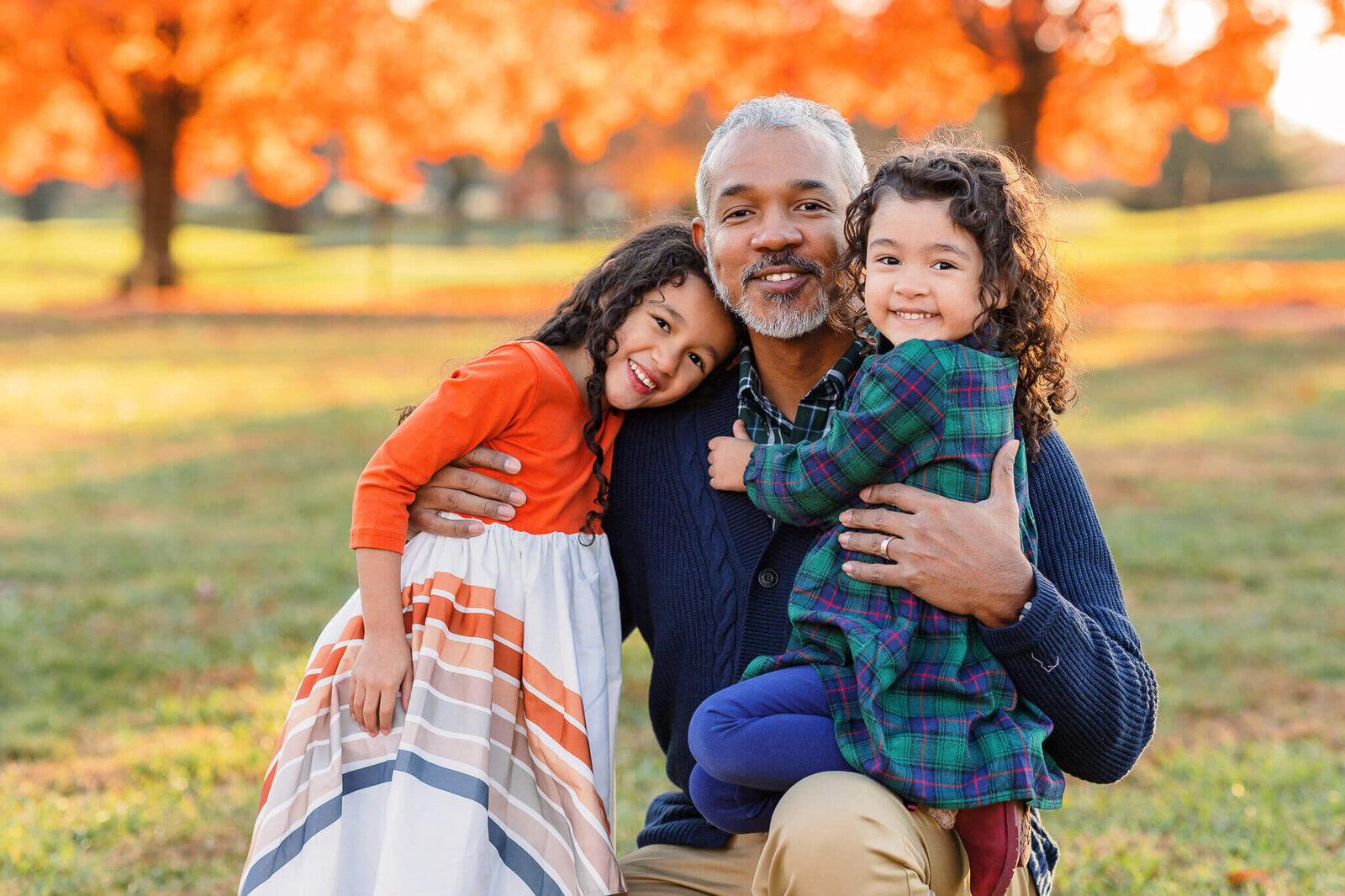 A dad kneeling on the ground and hugging his two daughters