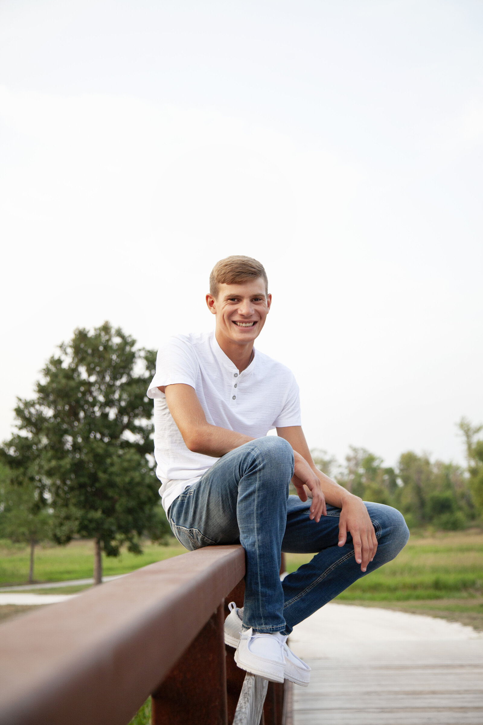 Senior boy sitting on bridge railing, similing.