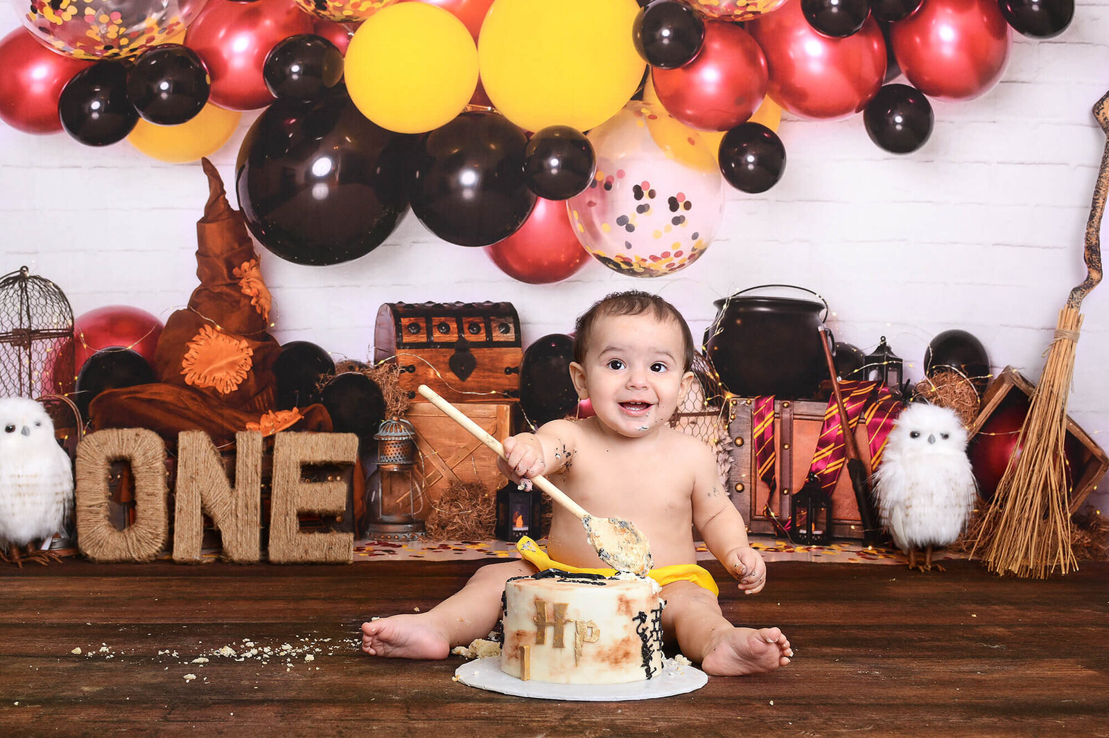 boy holds a spoon above his harry potter themed cake at his first birthday photoshoot in houston texas
