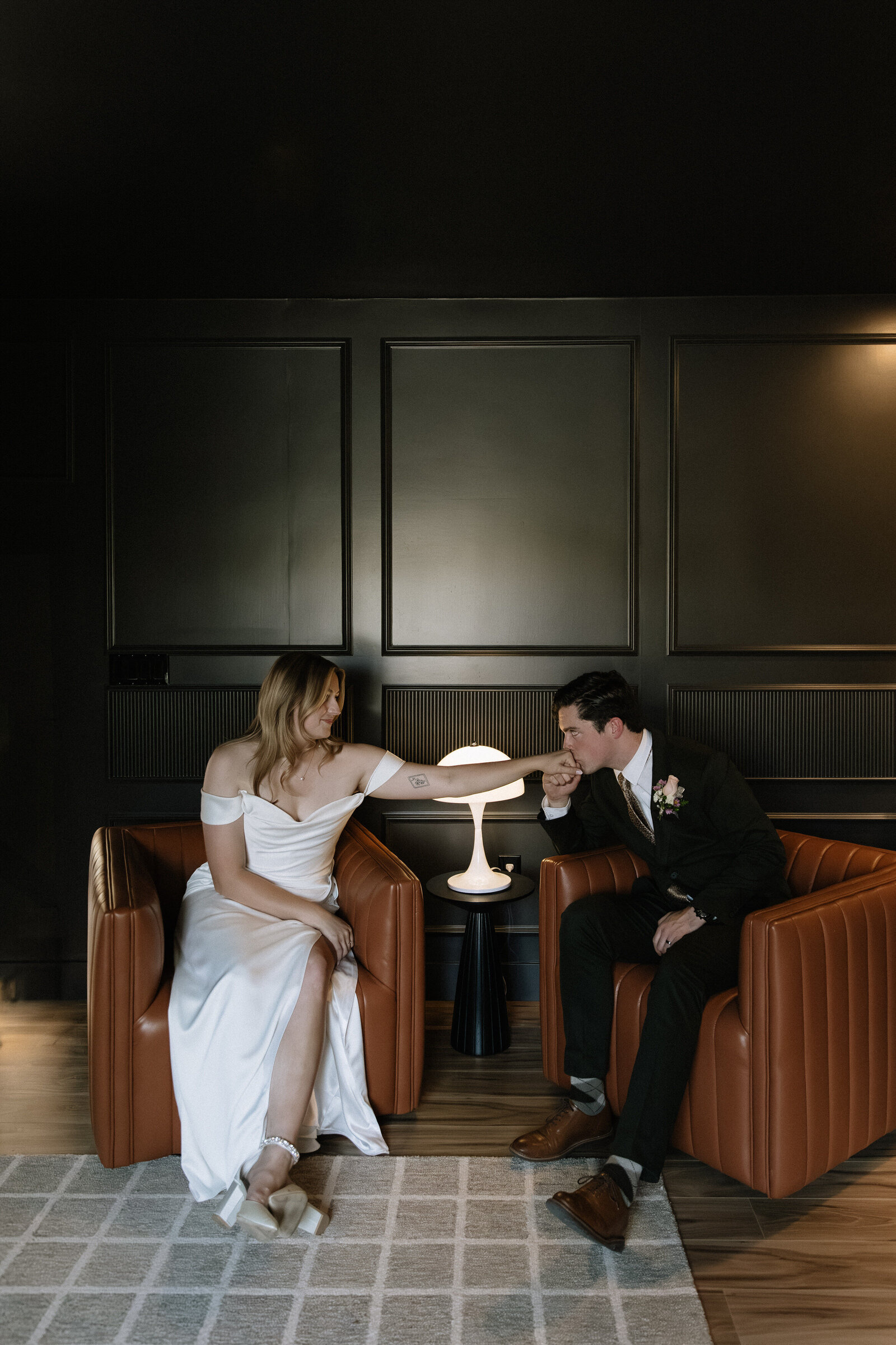 Groom reaching over to kiss bride's hand in intimate moment while they sit across from each other
