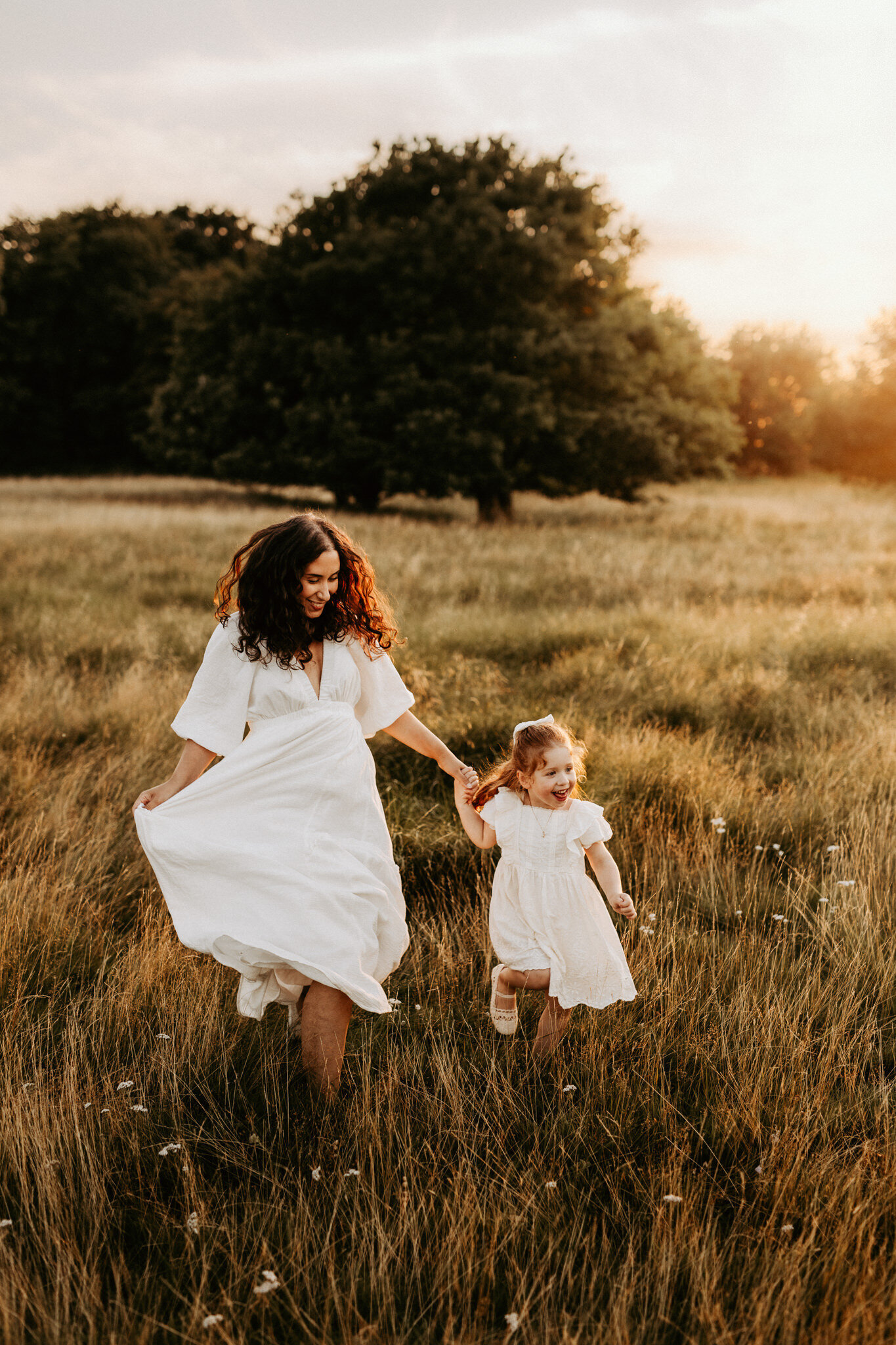 en mamma och dotter springer på ett fält i vita klänningar