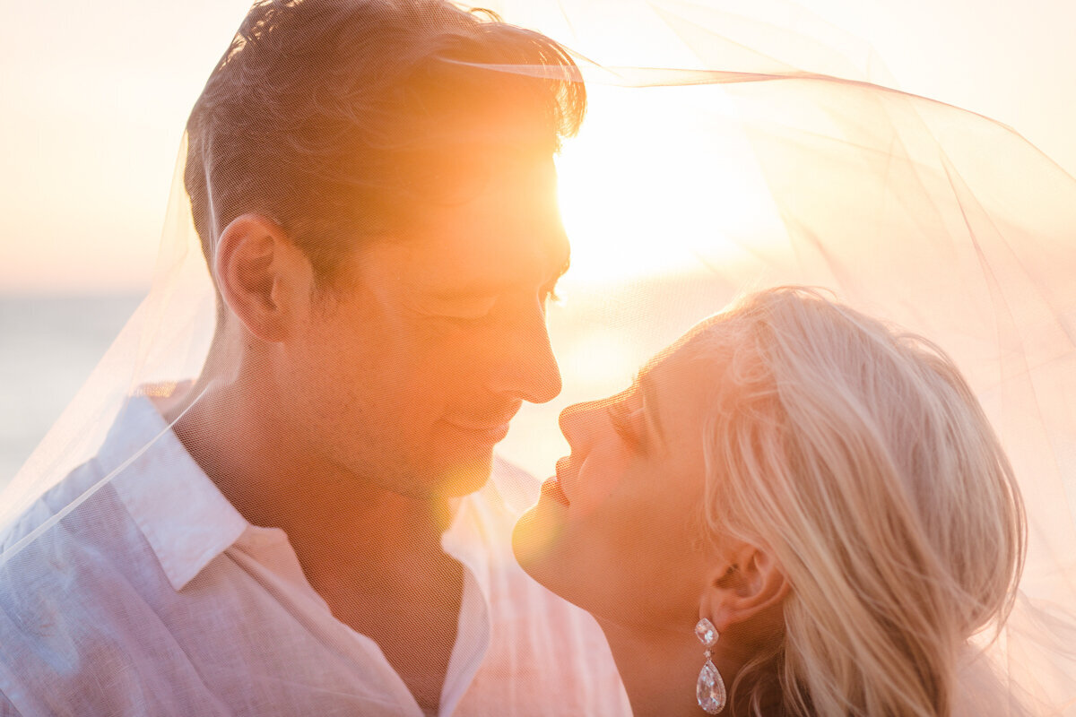 bride and groom looking at each other under the veil at sunset