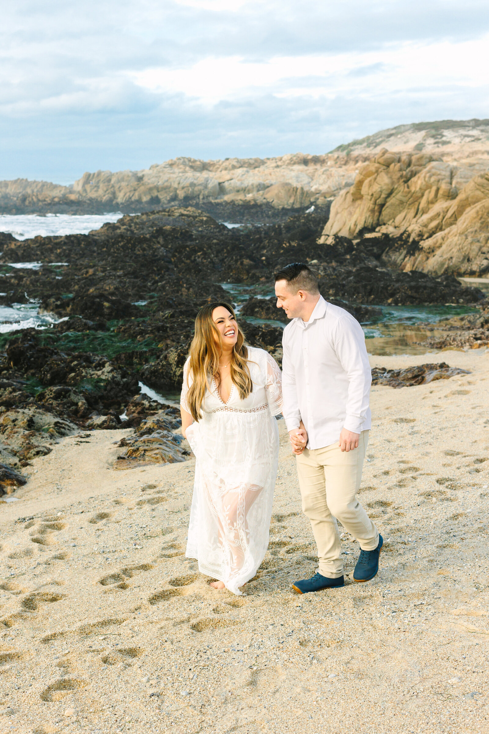 An engaged man and woman take photos on the beach in Pacific Grove, Monterey, California near Big Sur.