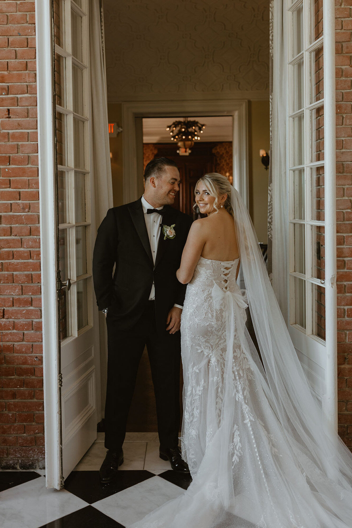 bride and groom standing in front of a doorway, smiling at each other