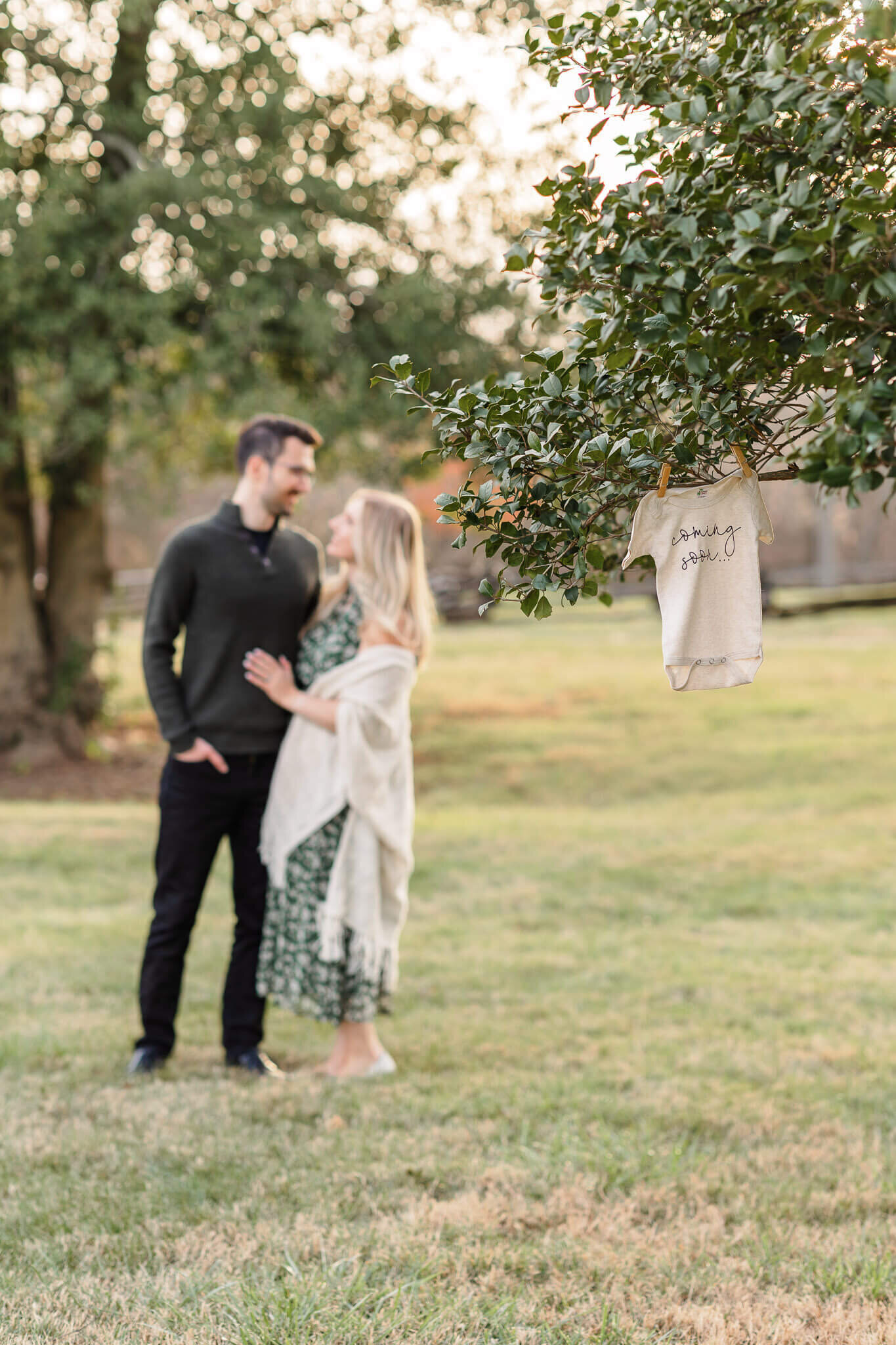 A baby onesie hanging in a tree while mom and dad hug in the background.