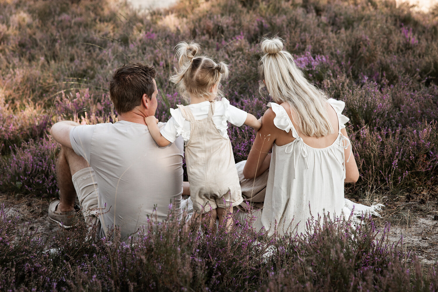 Een jong meisje staat tussen haar ouders tijdens een ongedwongen gezinsshoot in de natuur.