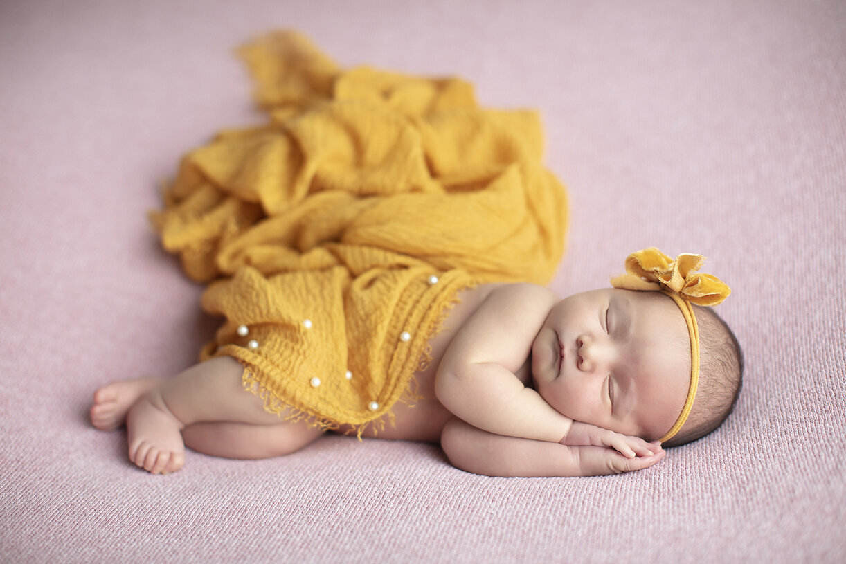 Newborn girl on pink with yellow scarf.