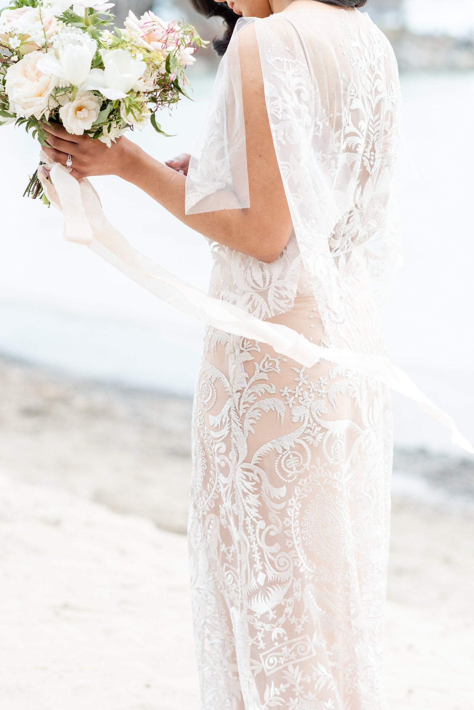 Bride-in-a-lace-wedding-dress-walking-along-the-beach-with-her-bouquet