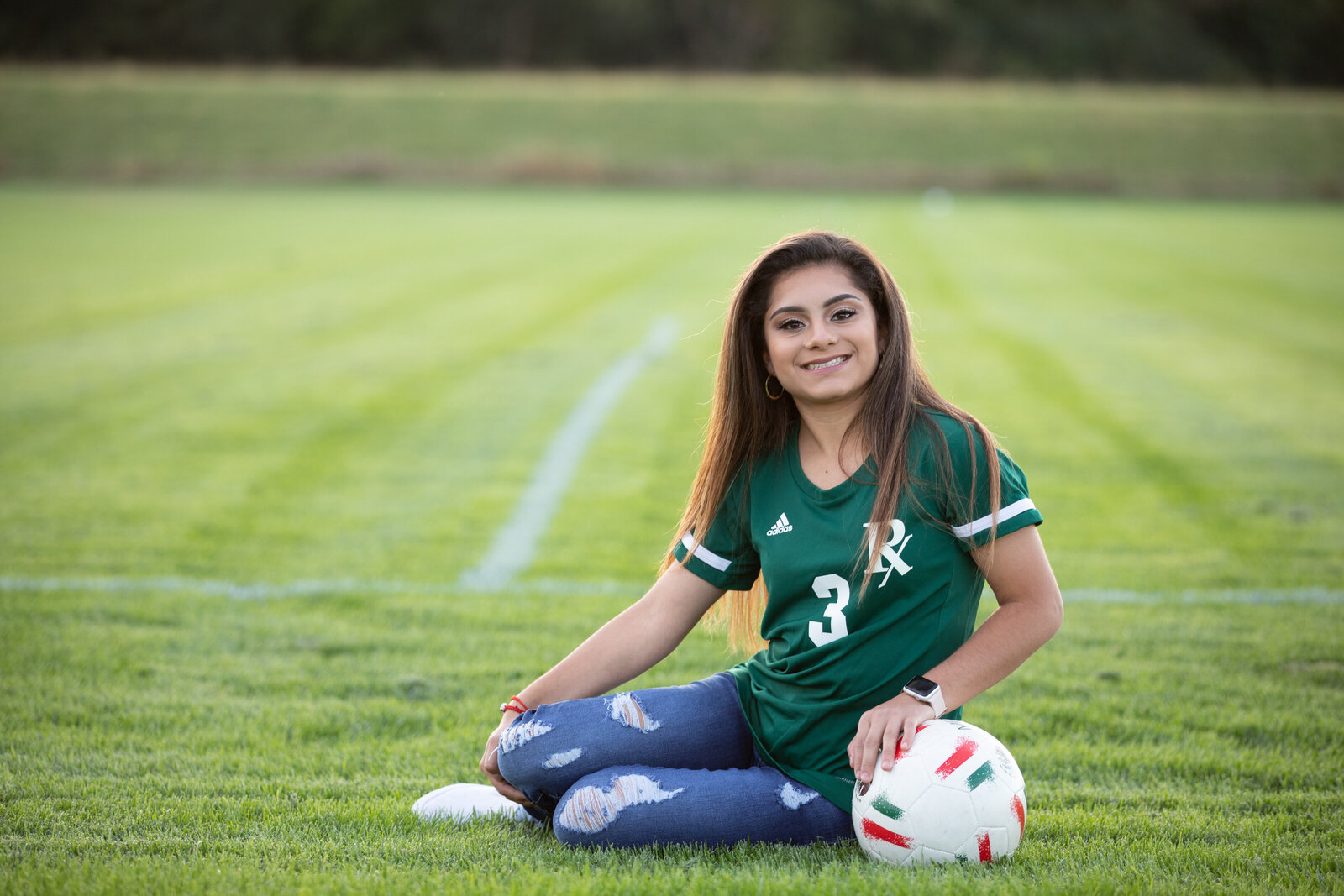 Senior sits in a soccer field with her ball