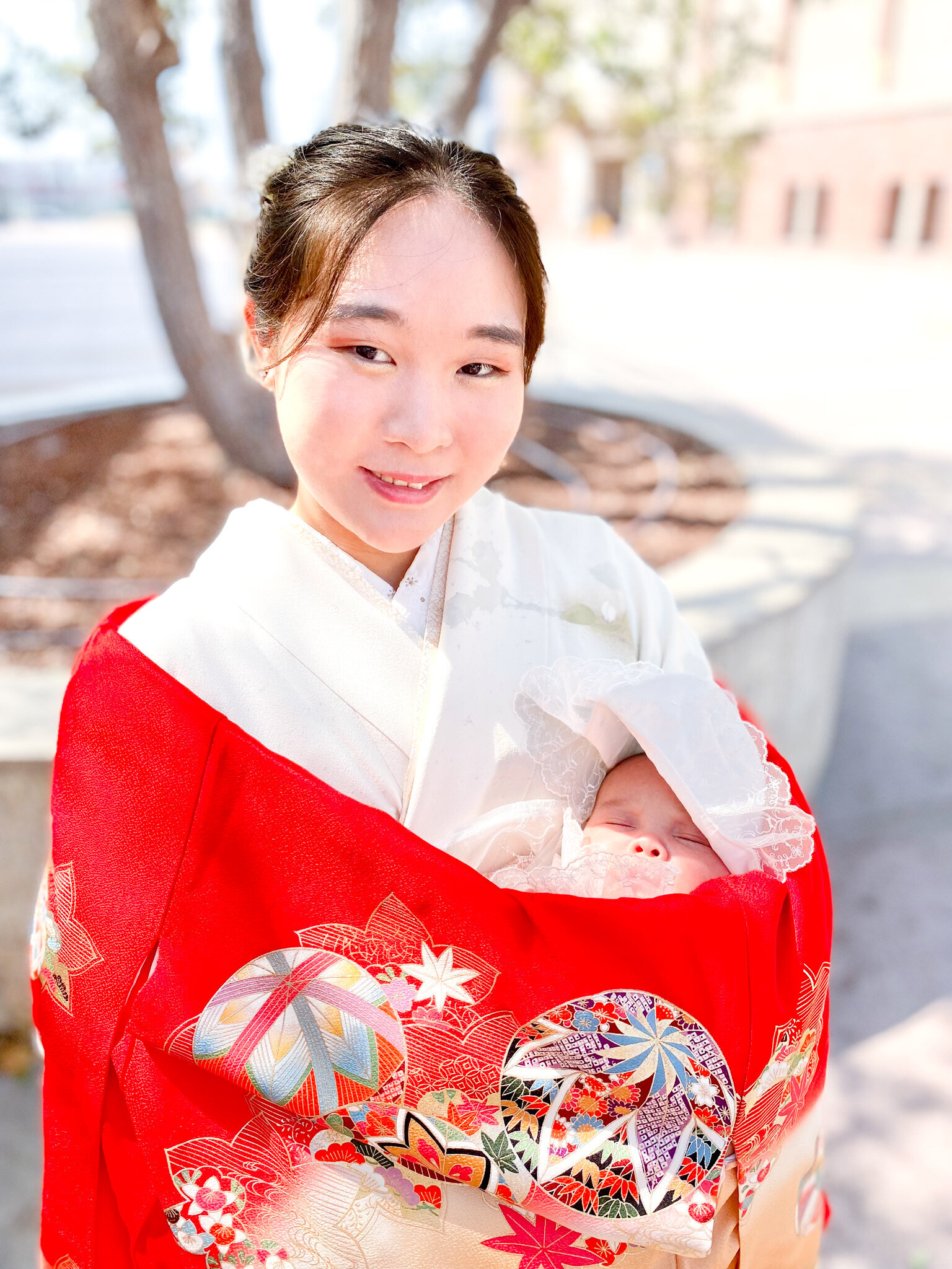 Mother smiling while holding baby wrapped in a vibrant red kimono during Hatsumairi ceremony | 初参り 母 赤い着物 赤ちゃん クローズアップ ロサンゼルス