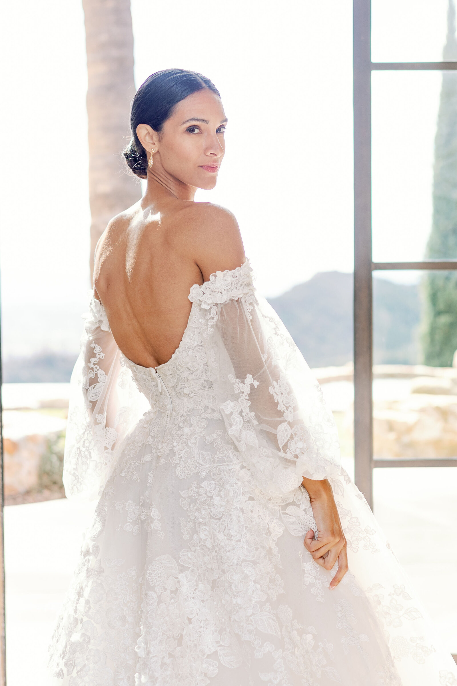 bridal portrait for California wedding with bride in a floral appliqué wedding dress holding the skirt and looking over her shoulder while wearing a slicked back bun captured by wedding photographer bay area