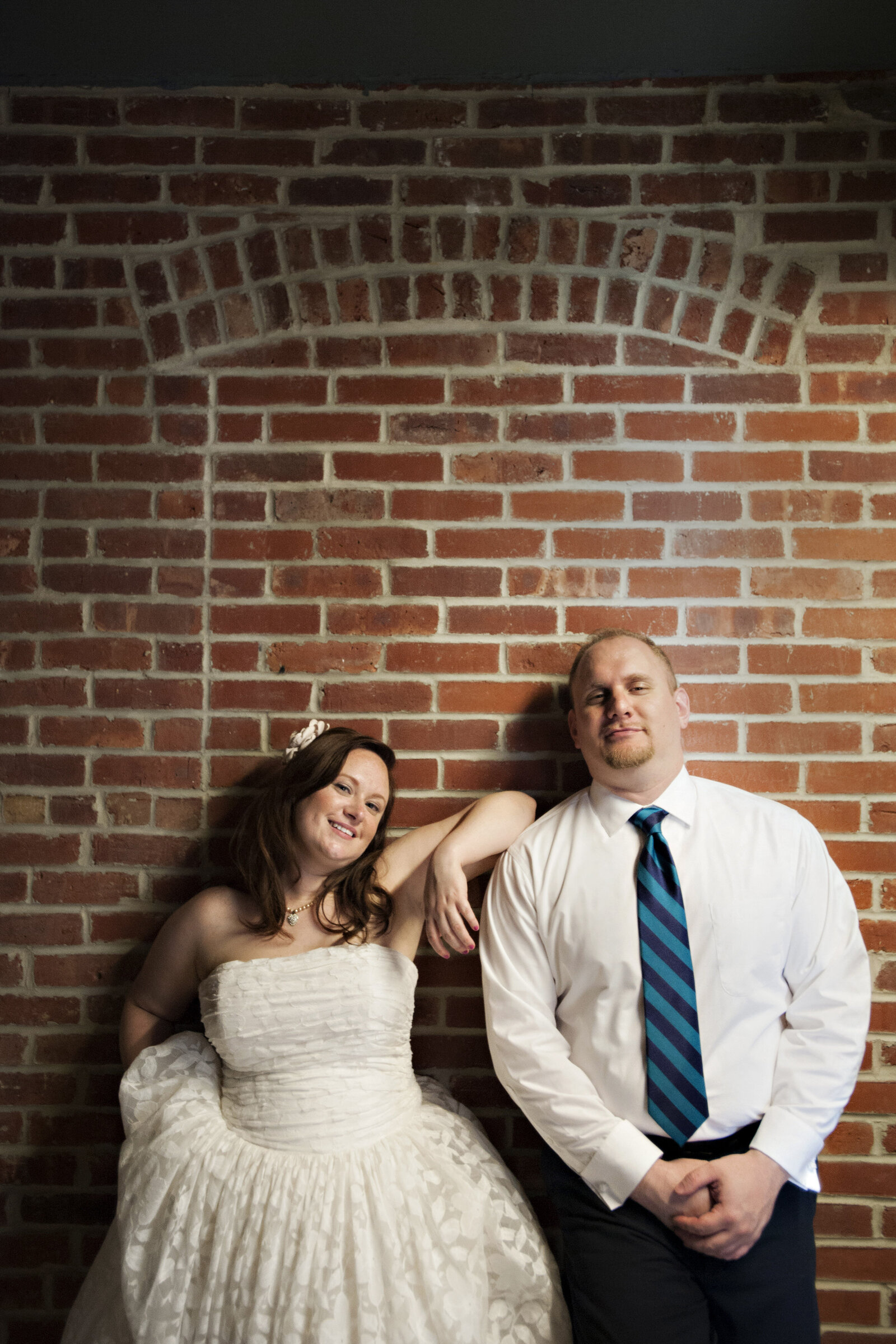 A newlywed couple casually standing together against a wall 
