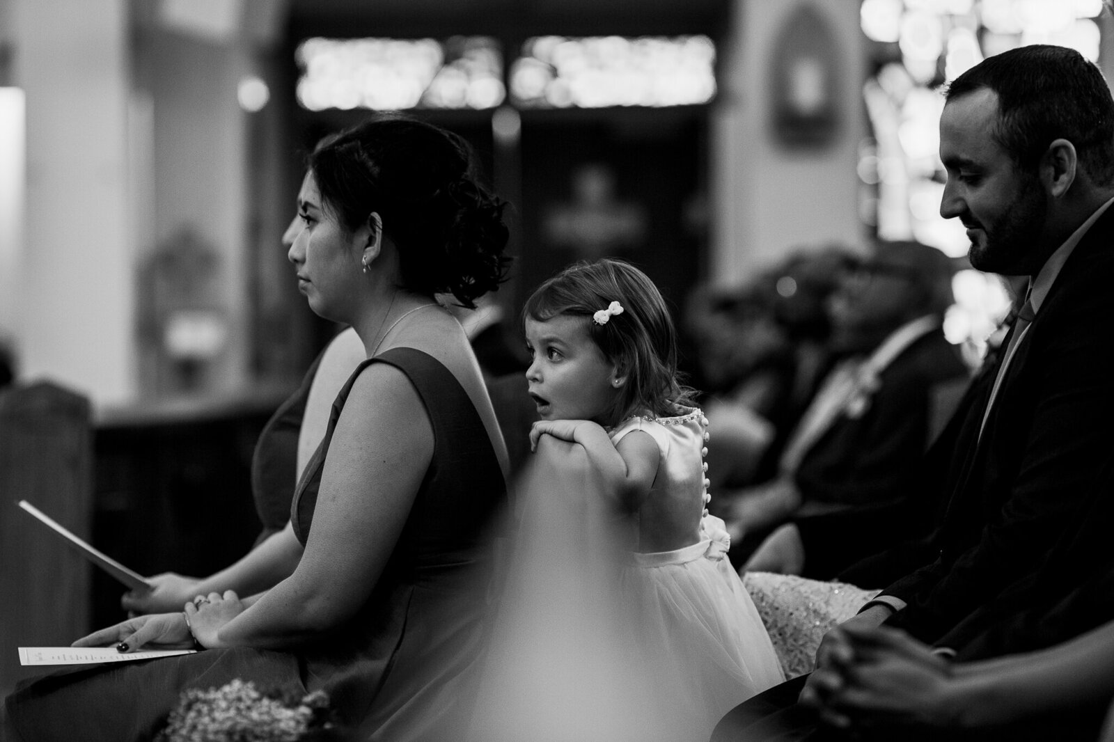 Flower girl looking over church pew during wedding ceremony in Brampton Ontario.