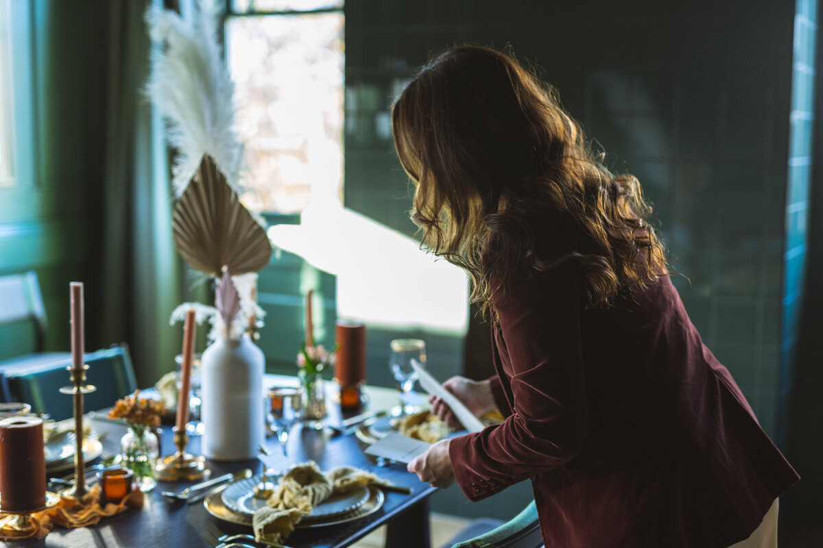 An event planner in Northwest Arkansas skillfully sets a dining table with plates, candles, and decorative items in a dimly lit room, creating an elegant atmosphere for a luxury event.