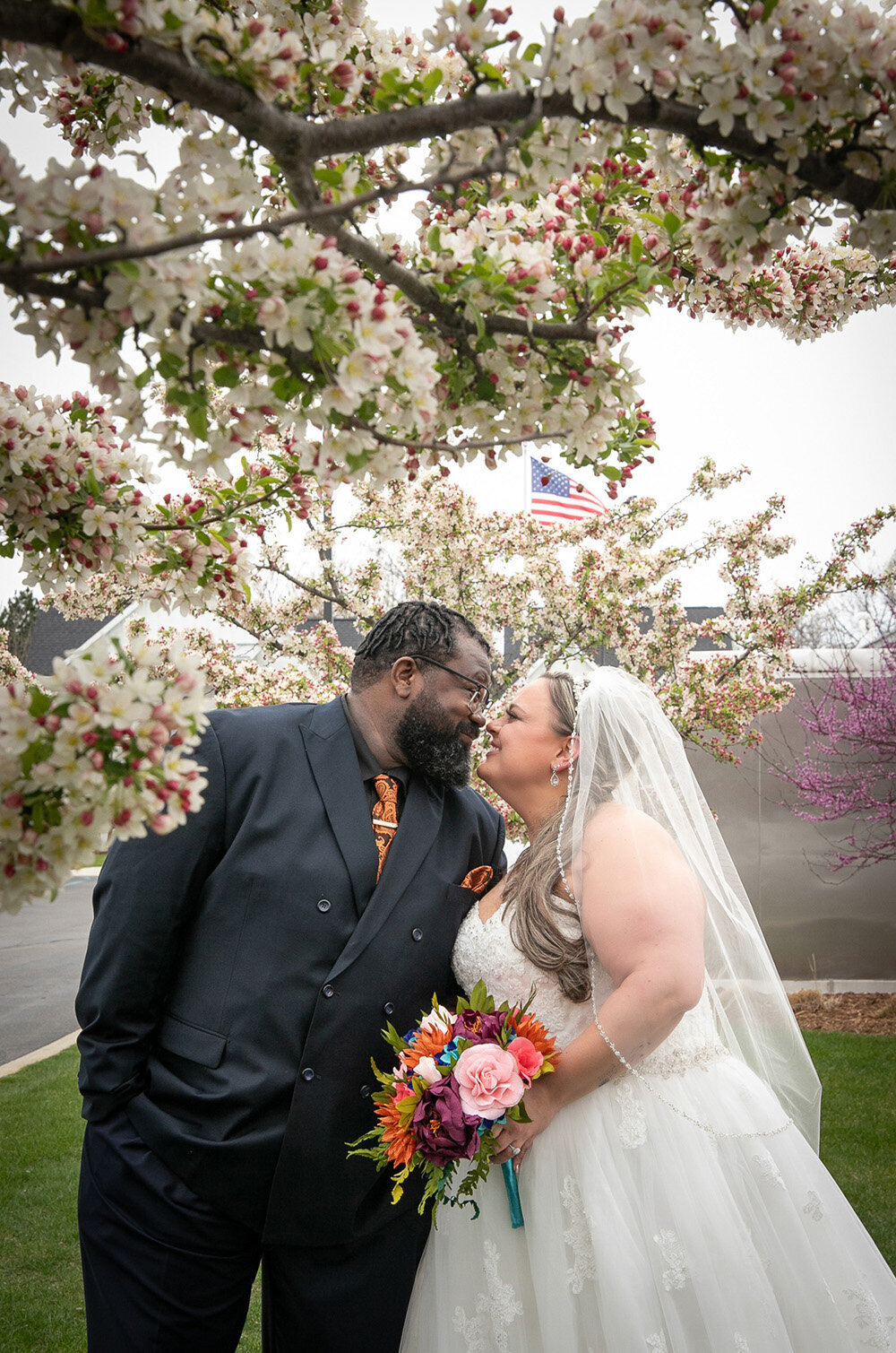 bride and groom put noses together under blossoming trees