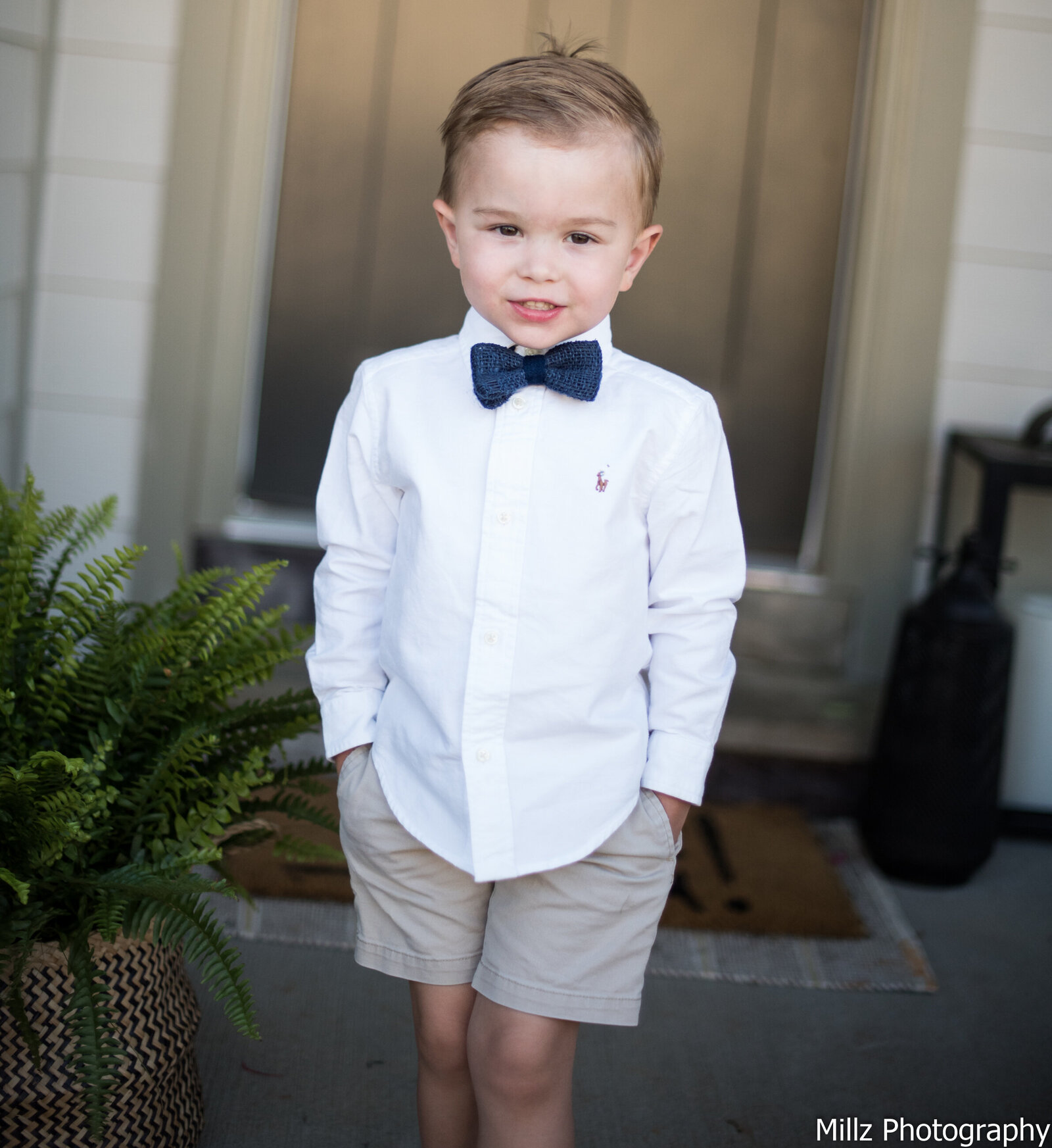 young boy in a dress shirt, bow tie, and shorts smiling for the camera photographed by Millz Photography in Greenville, SC