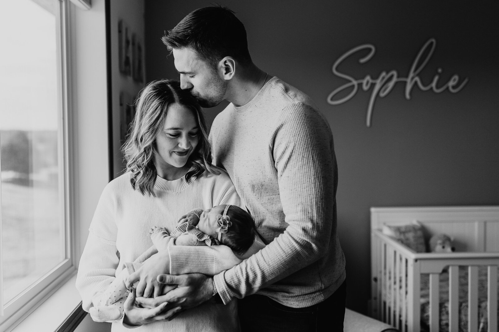 Woman holding newborn baby and man kissing the top of woman's head