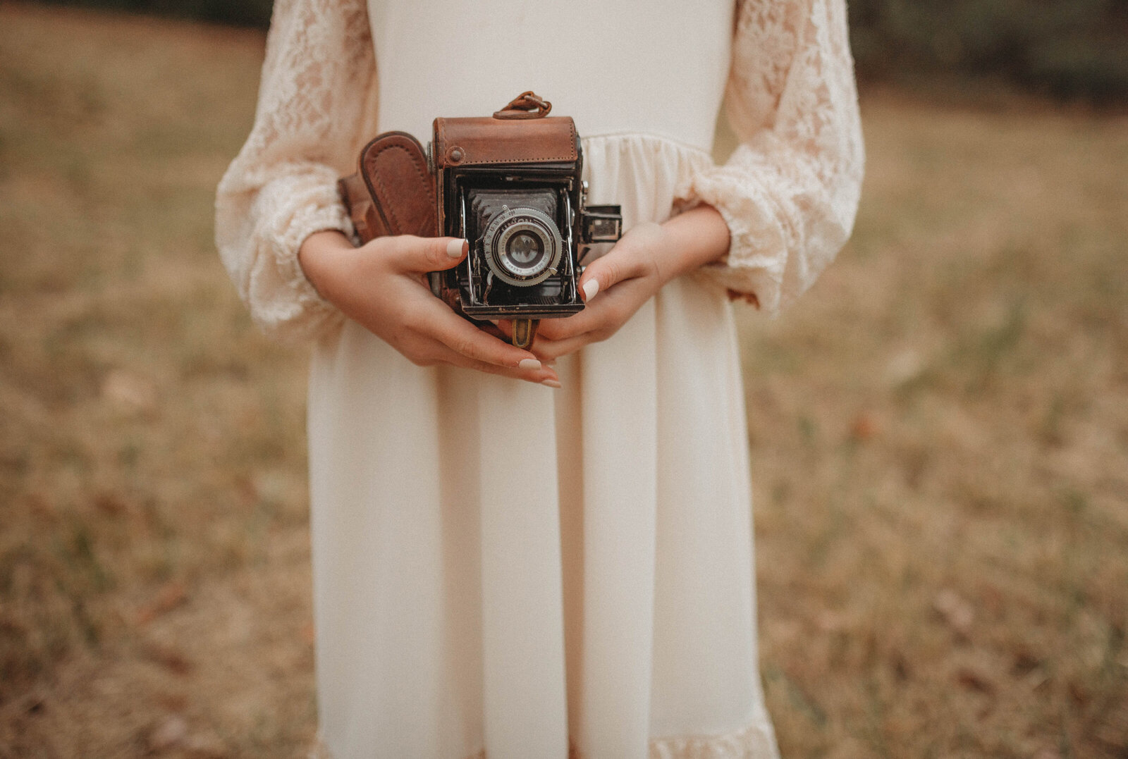 A vintage camera held by a woman in a lace dress, captured by Melena Lawson, a Blacksburg , Virginia, Photographer.