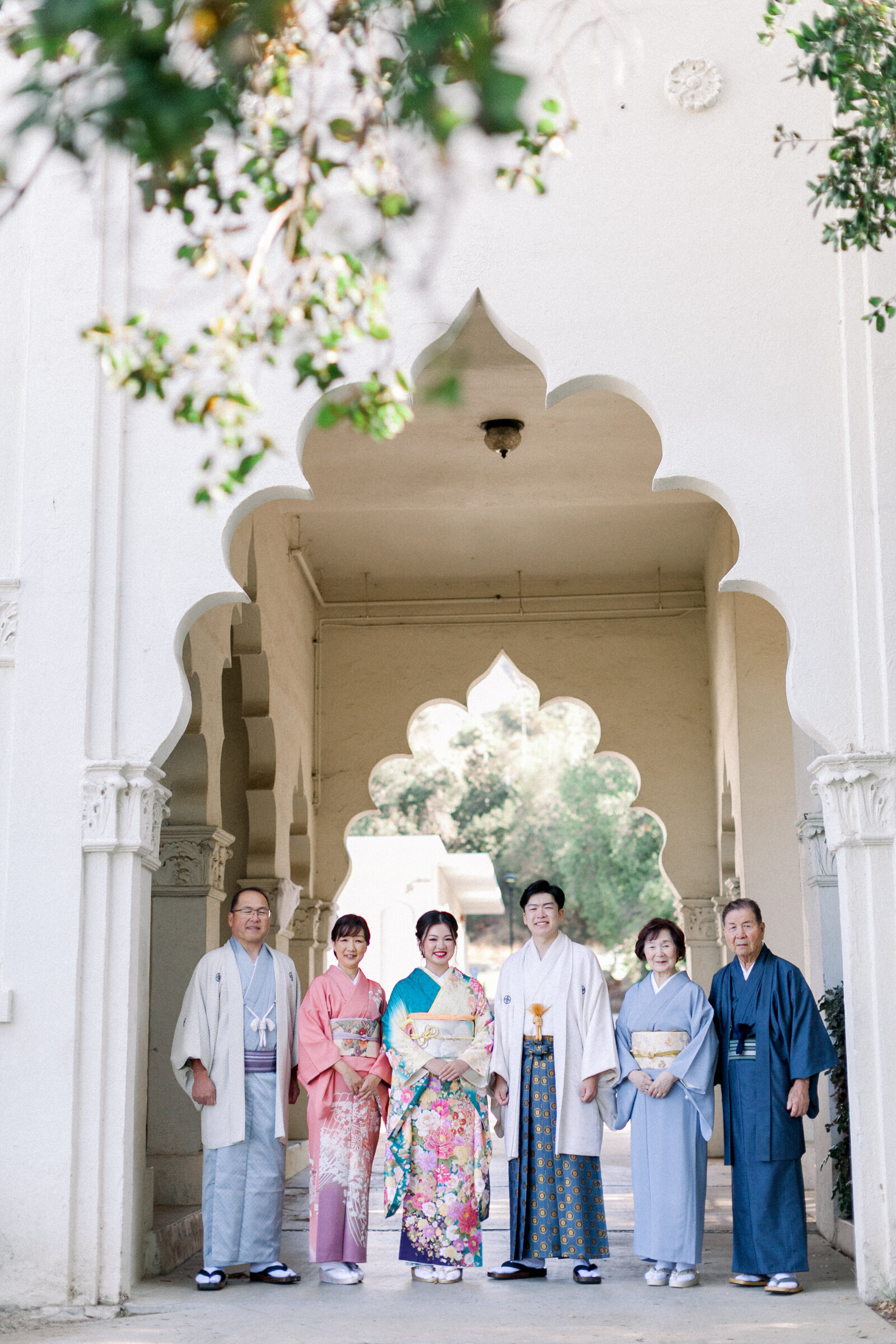 Full family group standing beneath the ornate archway of Brand Park Glendale for a Seijinshiki coming of age celebration, featuring a daughter in colorful furisode and a son in hakama, kimono rental Los Angeles
ロサンゼルス グレンデールのブランドパーク 装飾アーチの下で成人式を祝う家族全員の集合写真 振袖の娘と袴姿の息子 着物レンタル
