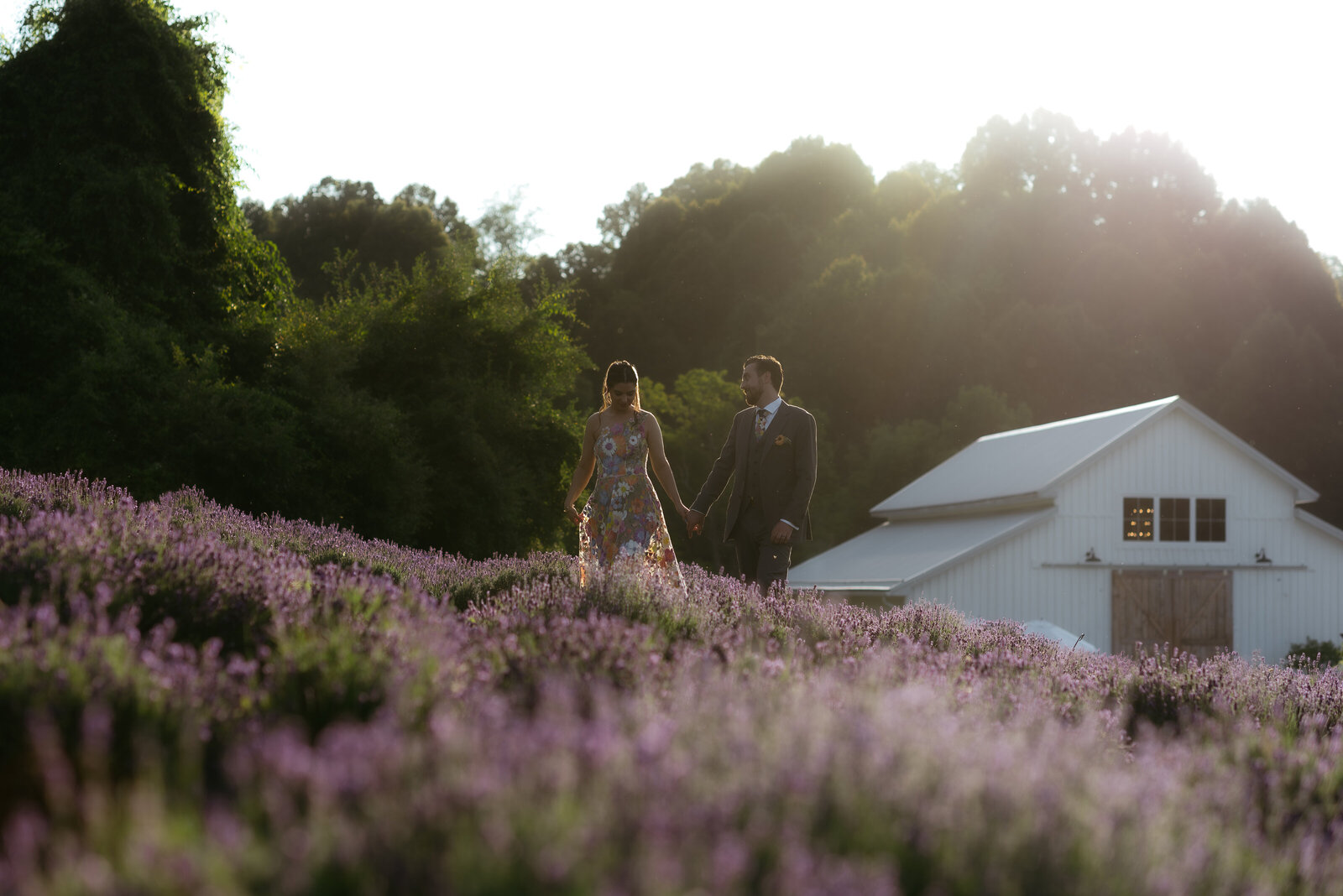 A bride in a rainbow flower dress and her groom walk the Stone House Lavender blooms at sunset.